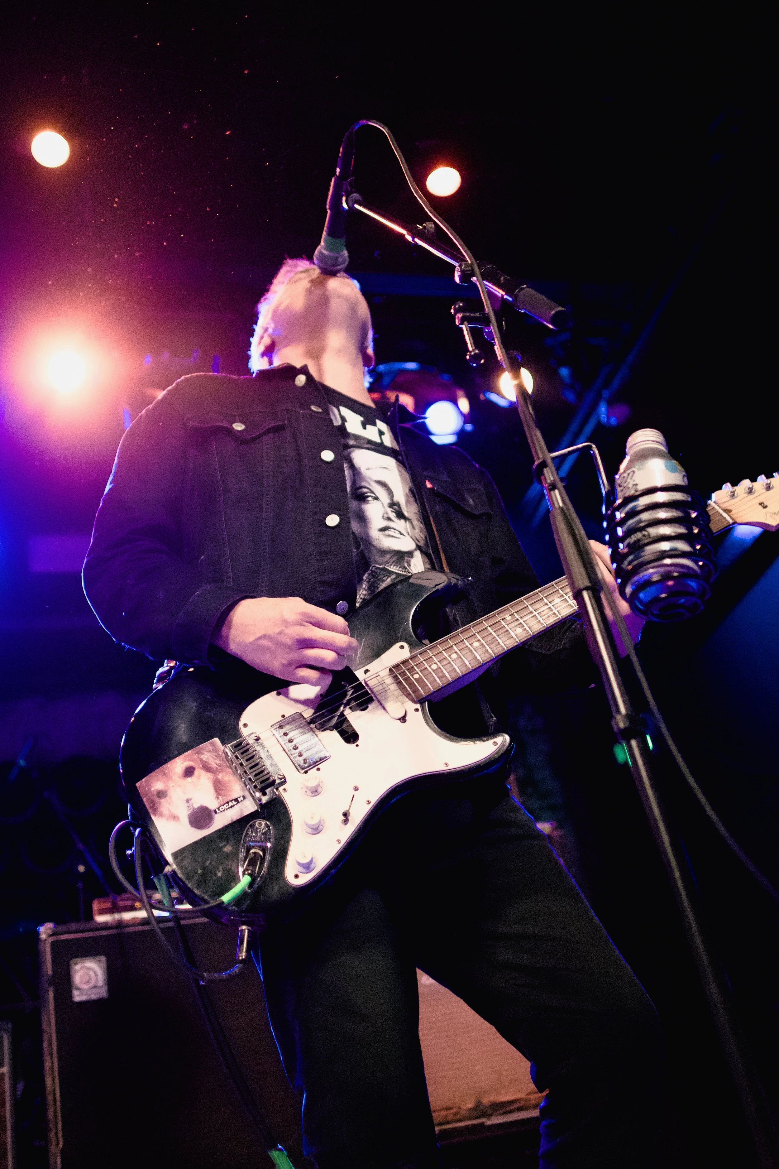 Musician performing on stage with an electric guitar under colorful stage lighting.