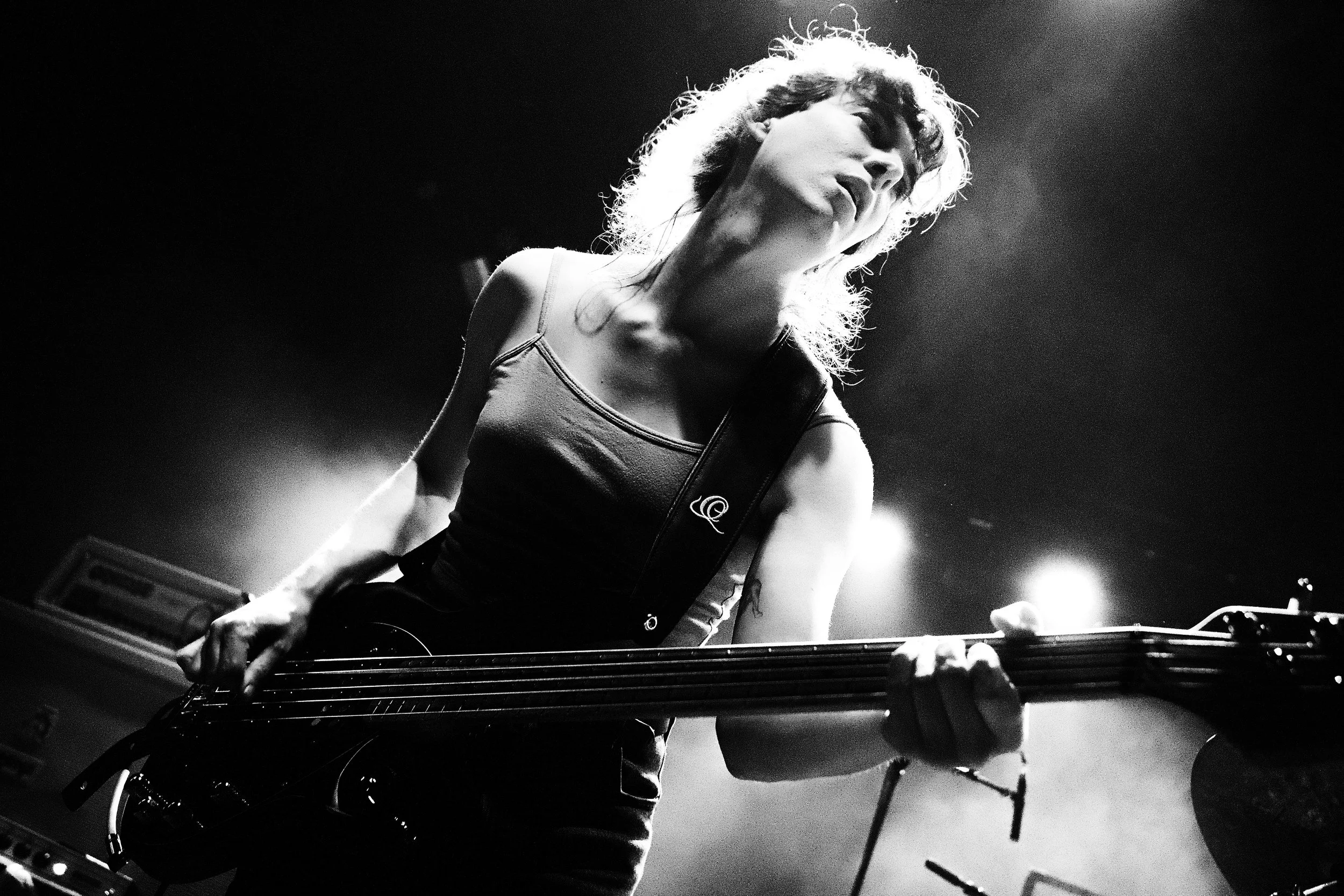 A woman playing an electric guitar on stage, illuminated by stage lights, in a black and white photo.