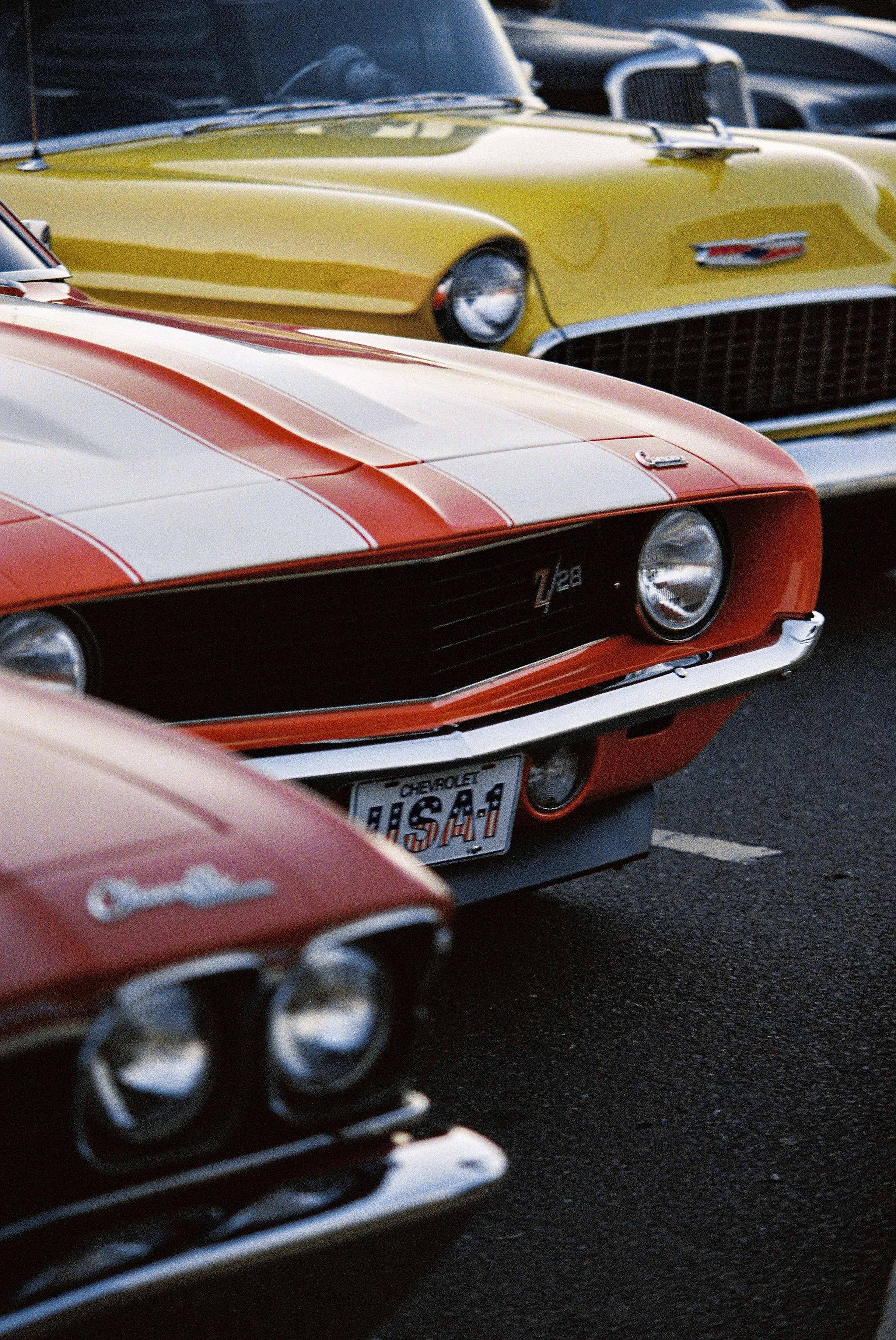 Close-up of vintage Chevrolet Corvettes parked together, featuring red, yellow, and orange colors at a car show.