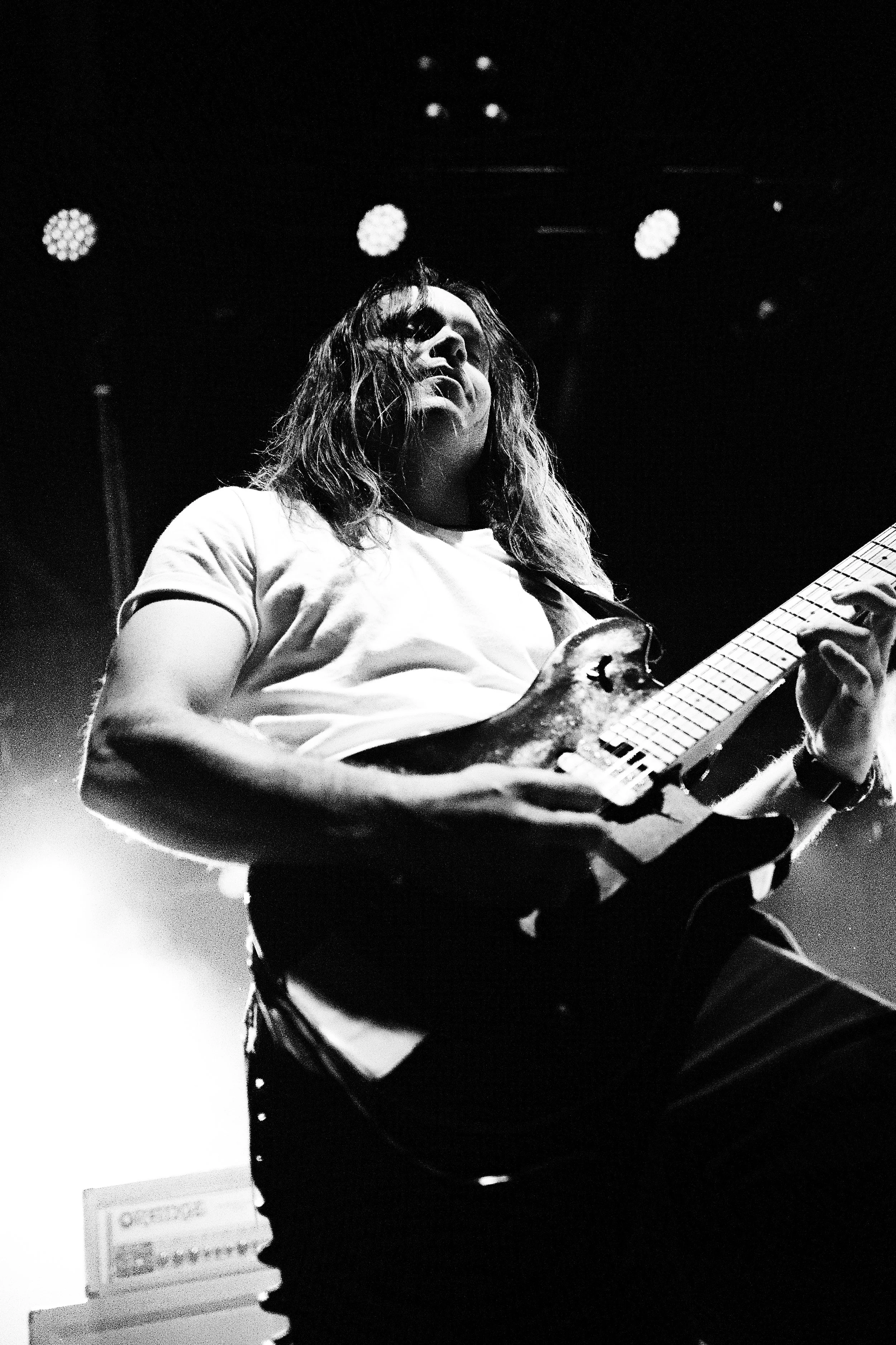 A musician with long hair playing an electric guitar on stage in black and white.