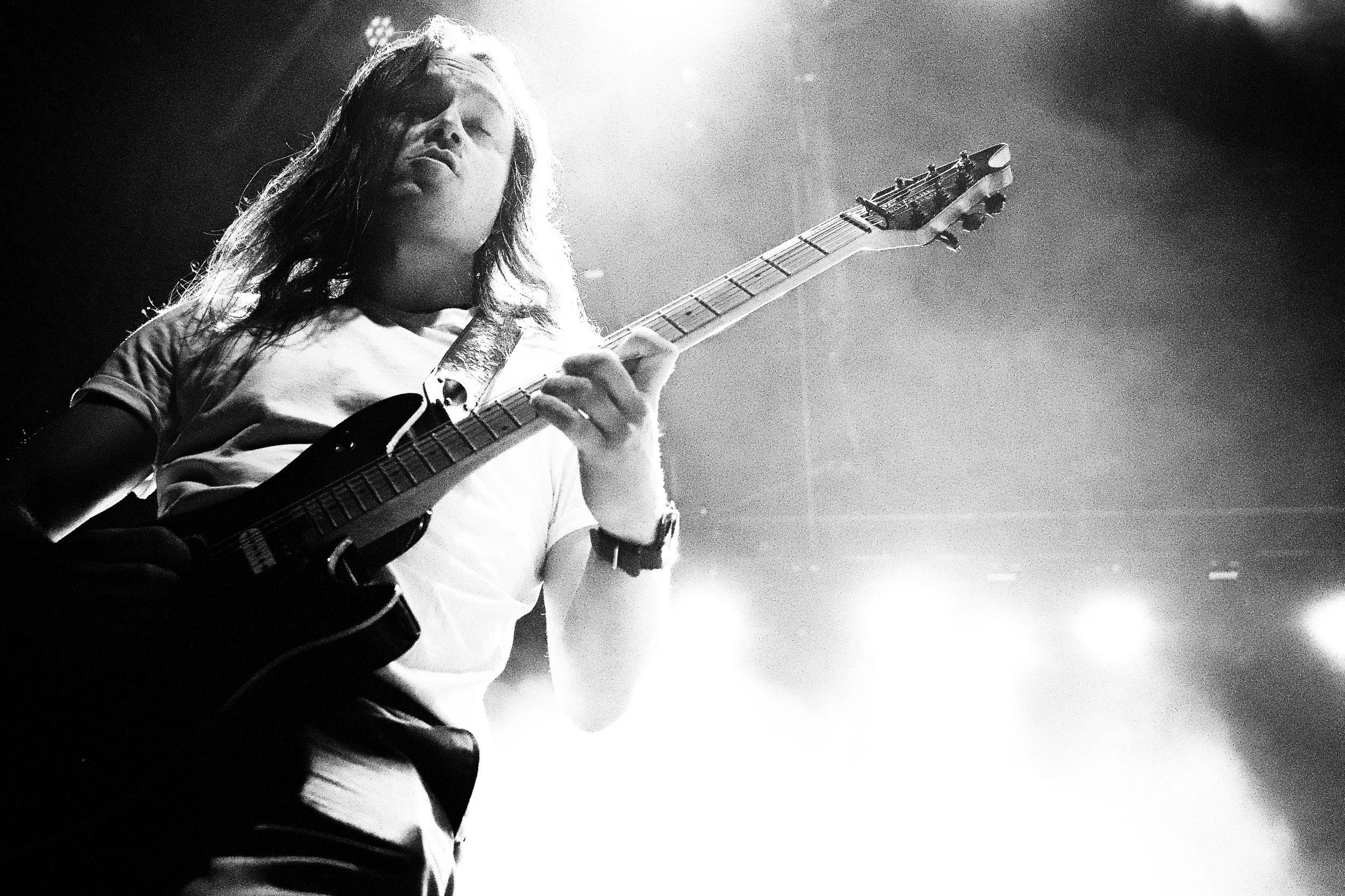 A young woman playing an electric guitar on stage, illuminated by bright lights, in black and white.