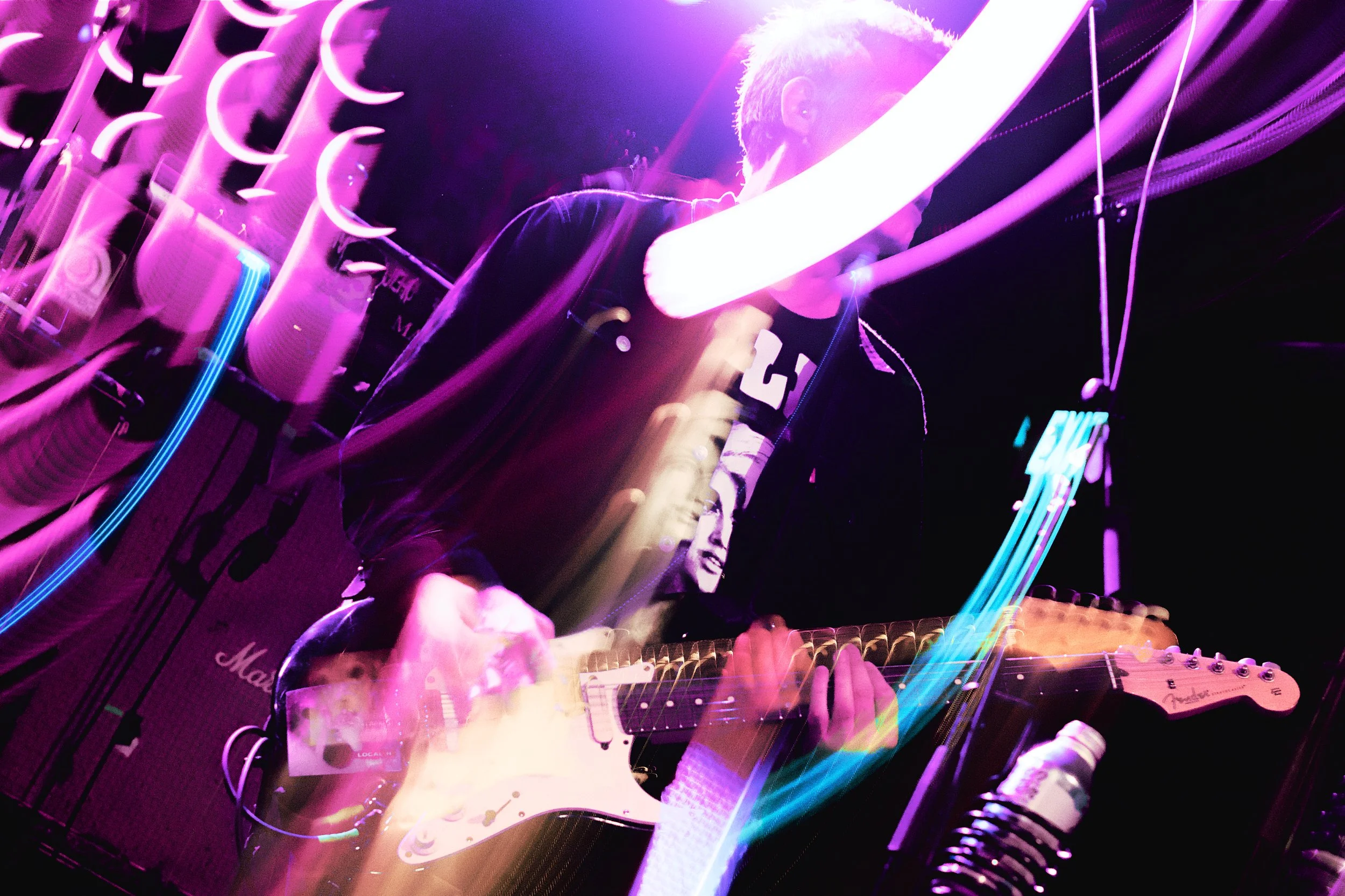 A person playing an electric guitar on stage with colorful neon light effects.
