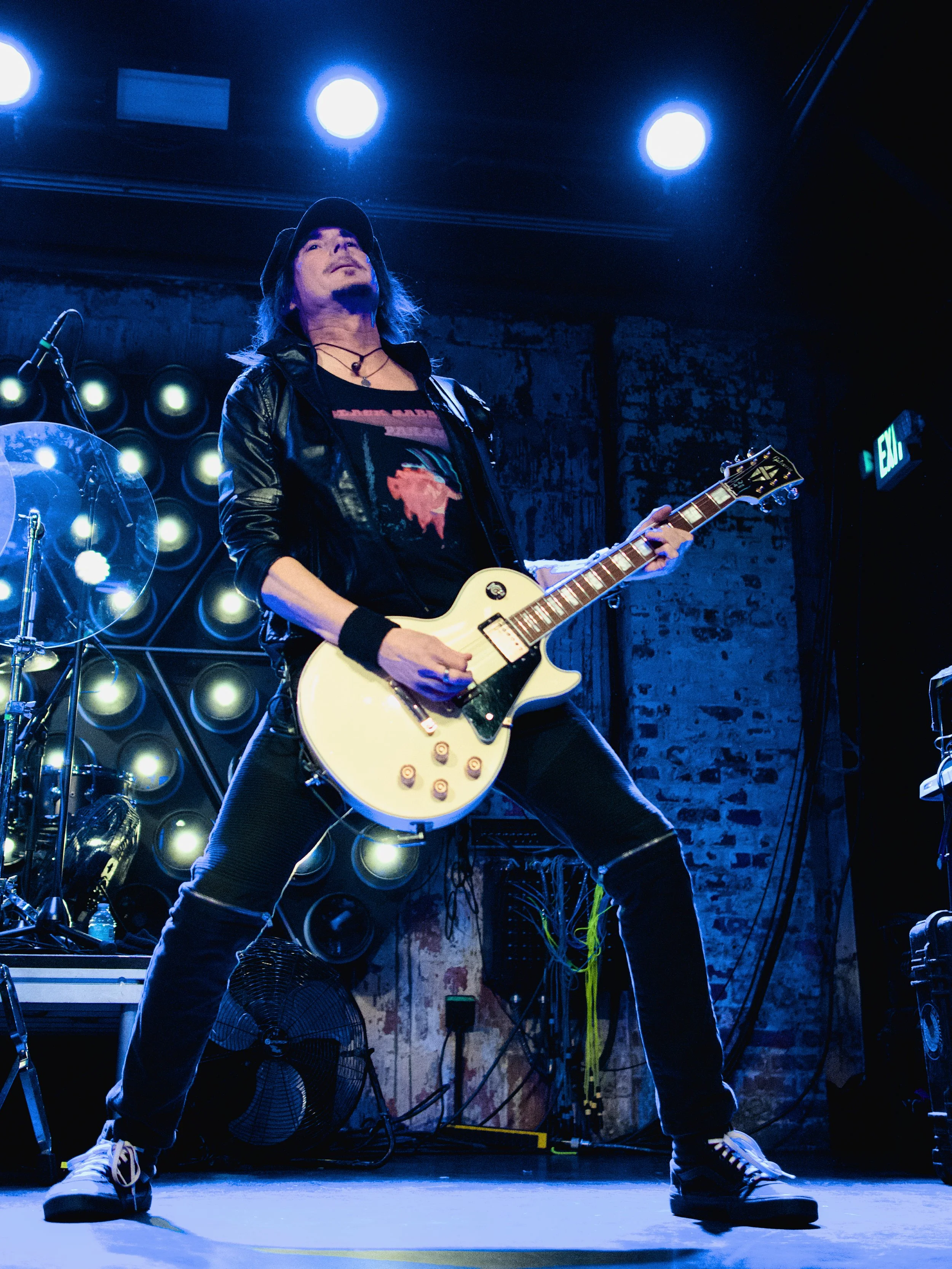 Guitarist performing on stage with blue lighting and industrial background.