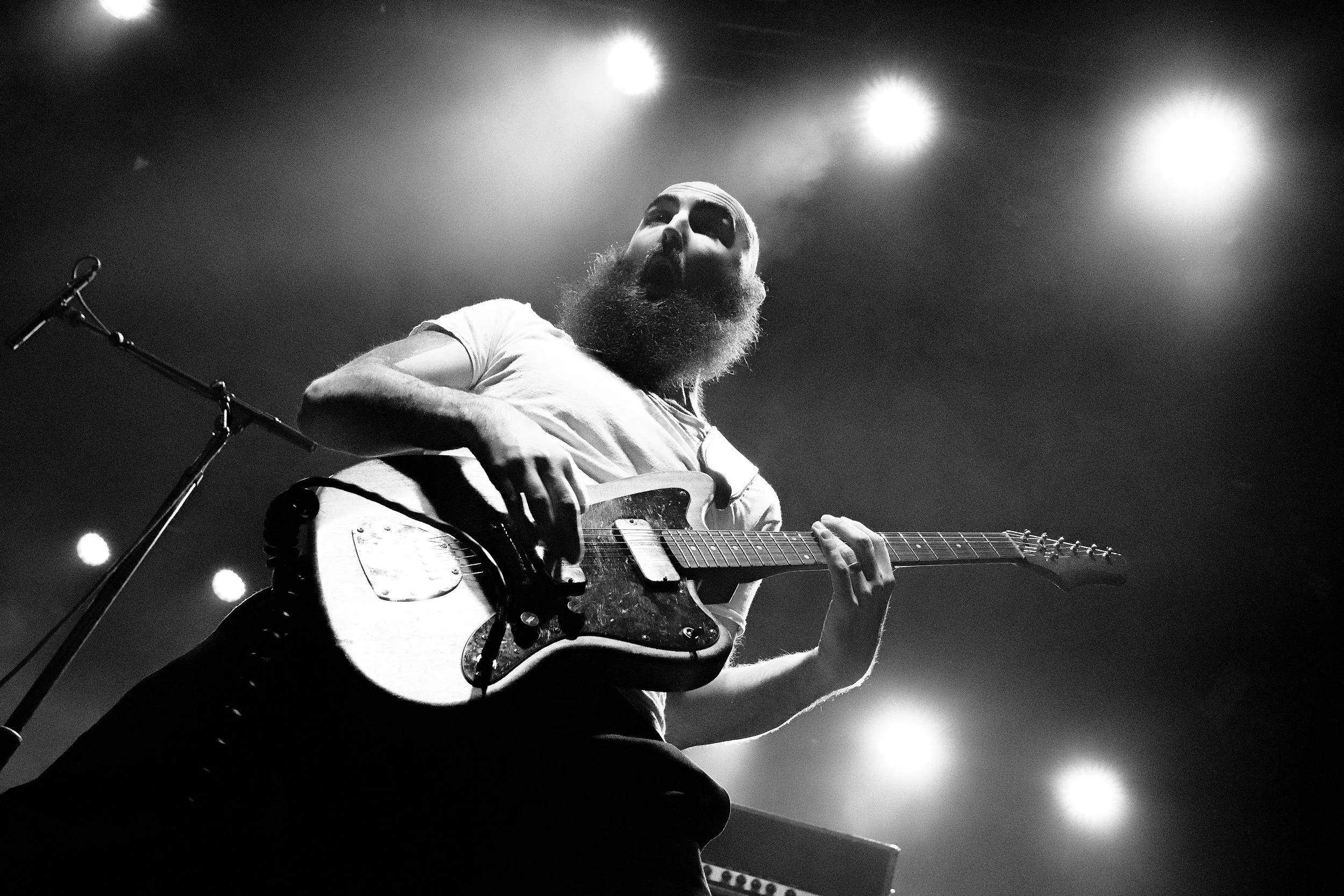 A bearded musician with painted face playing an electric guitar on stage during a concert.
