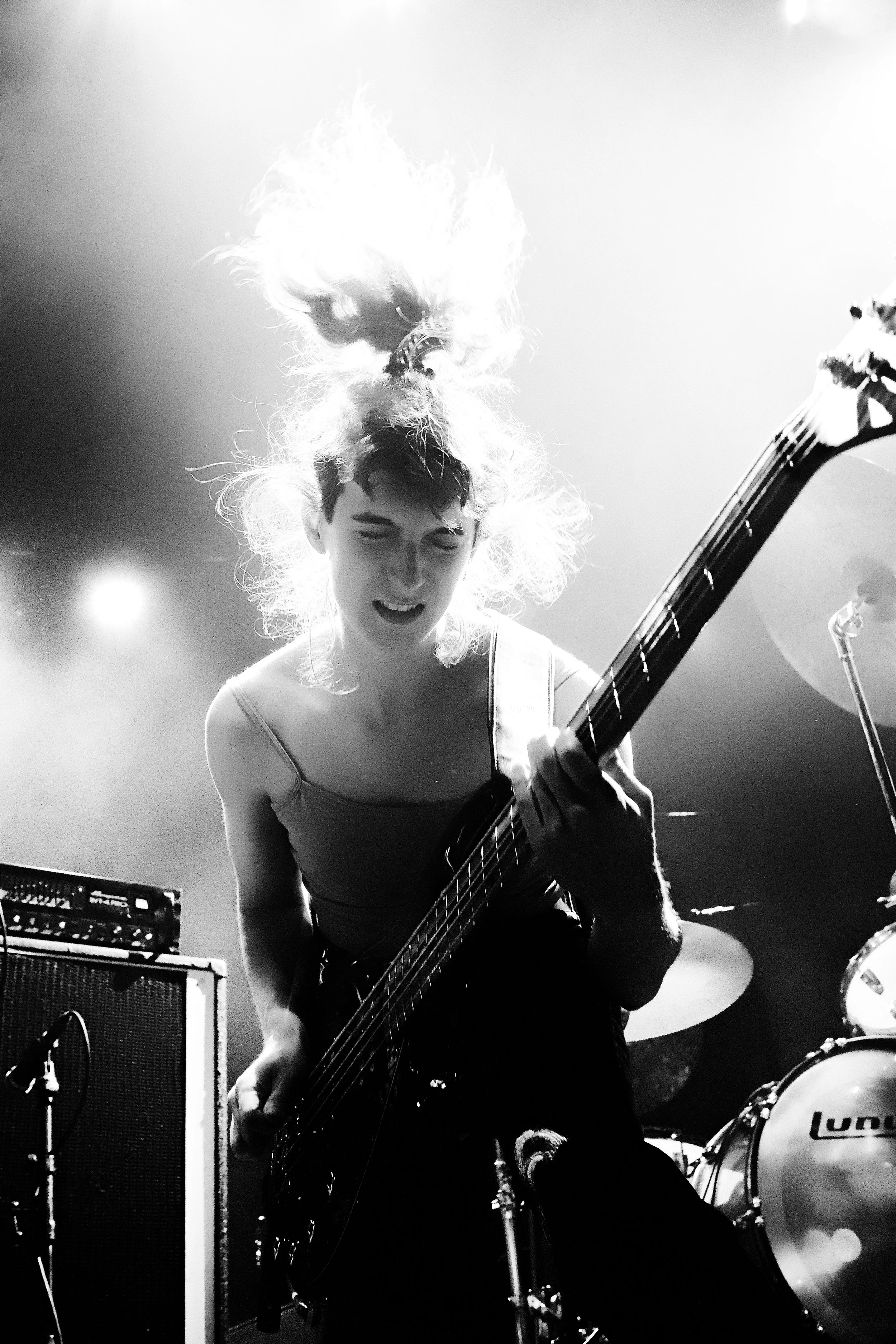 A woman playing an electric guitar on stage, with wild hair and an intense expression, in black and white.