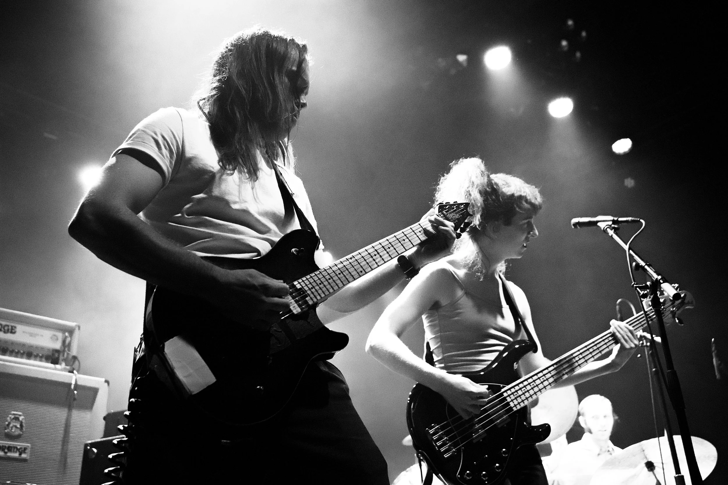 Two female musicians playing guitars on stage during a concert with stage lights in the background.