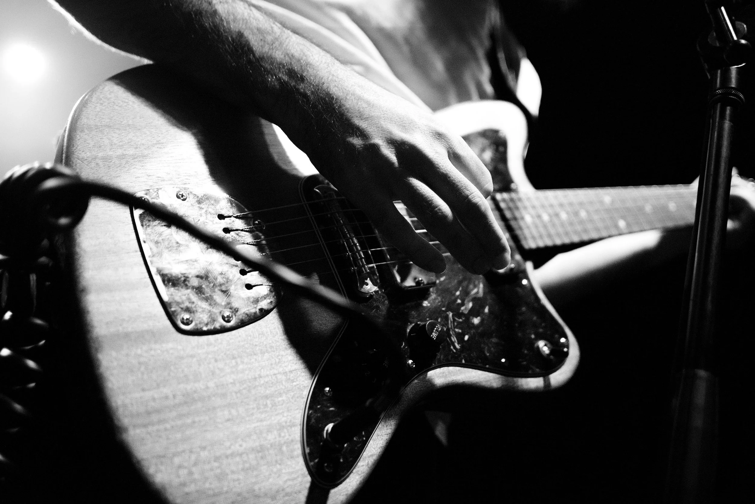 A person playing an electric guitar in black and white, focusing on their hand on the fretboard and the guitar body.