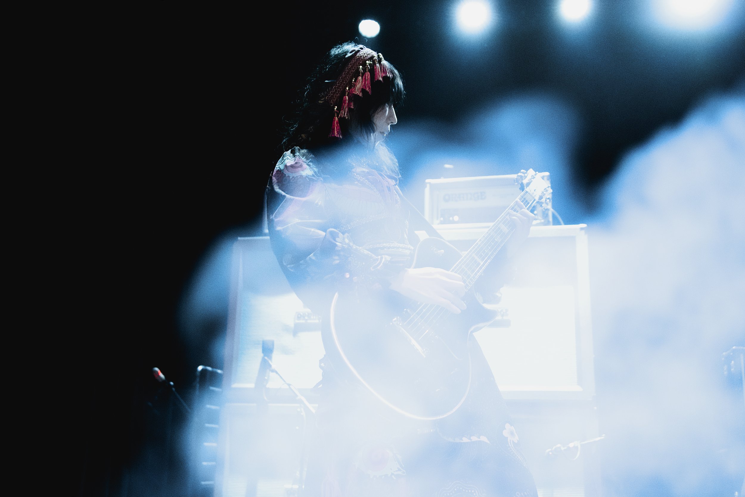 A woman playing an electric guitar on stage with bright blue lighting and smoke effects.