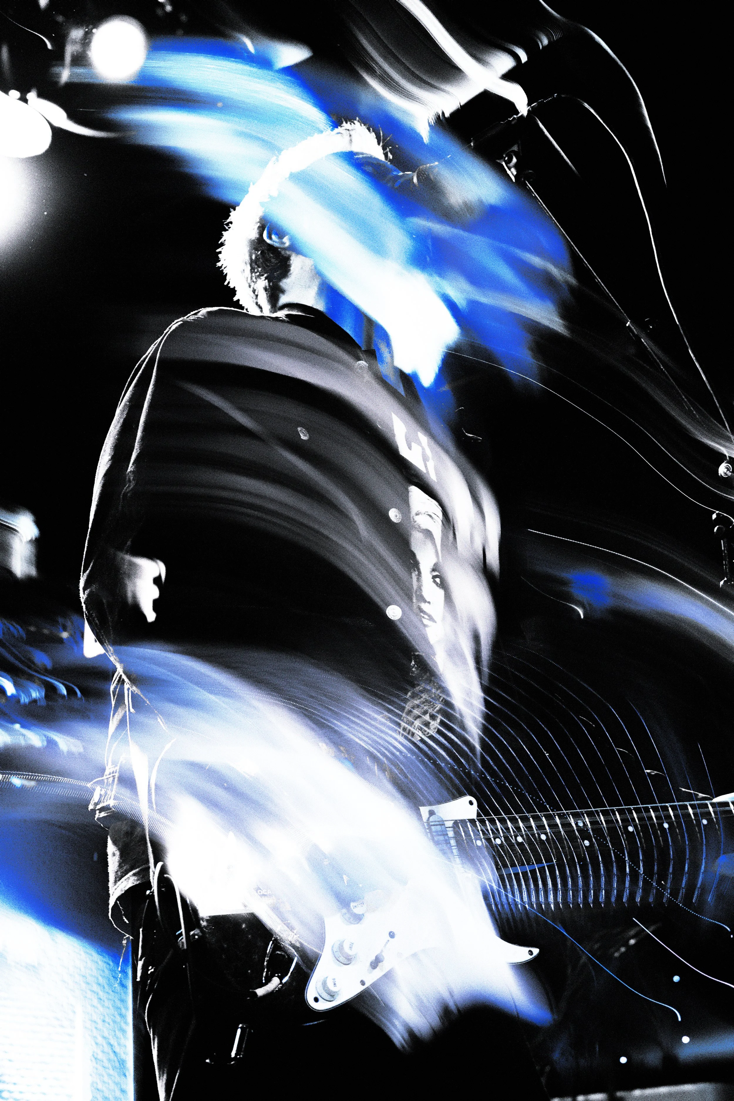 A person playing an electric guitar on stage with light streaks and a dark background.