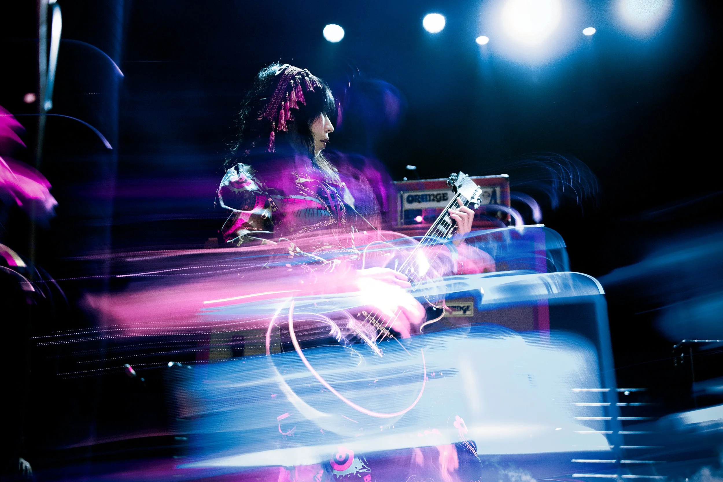 A woman playing an electric guitar on stage with colorful lights and effects.