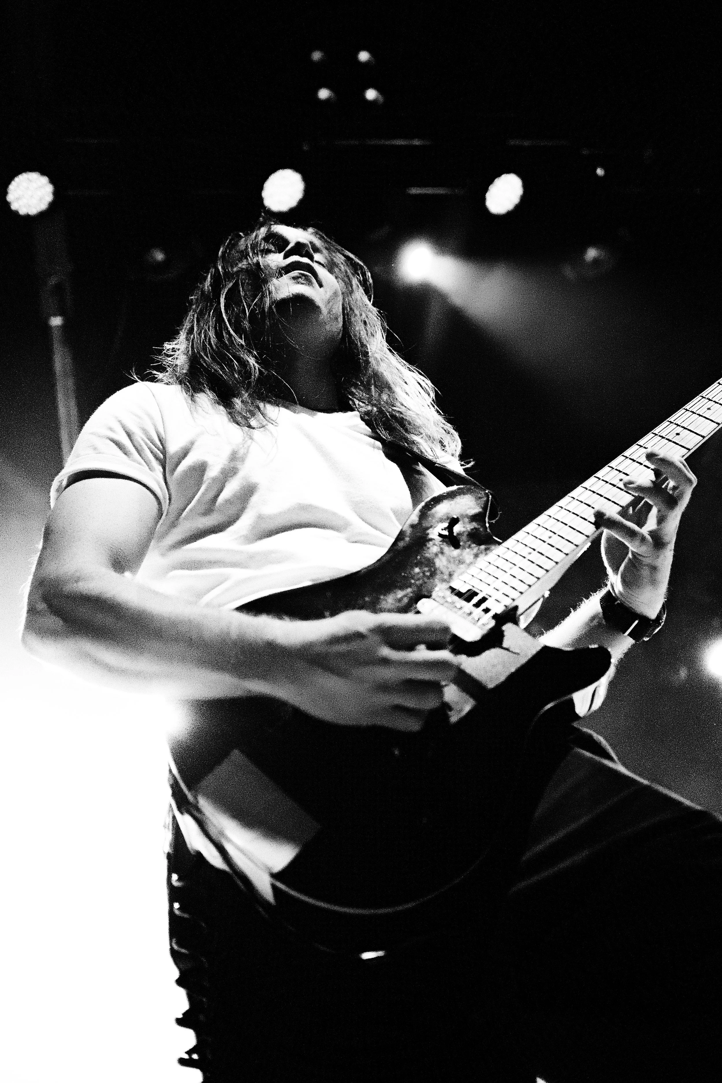 A black and white photo of a woman playing an electric guitar on stage, with stage lights around her.