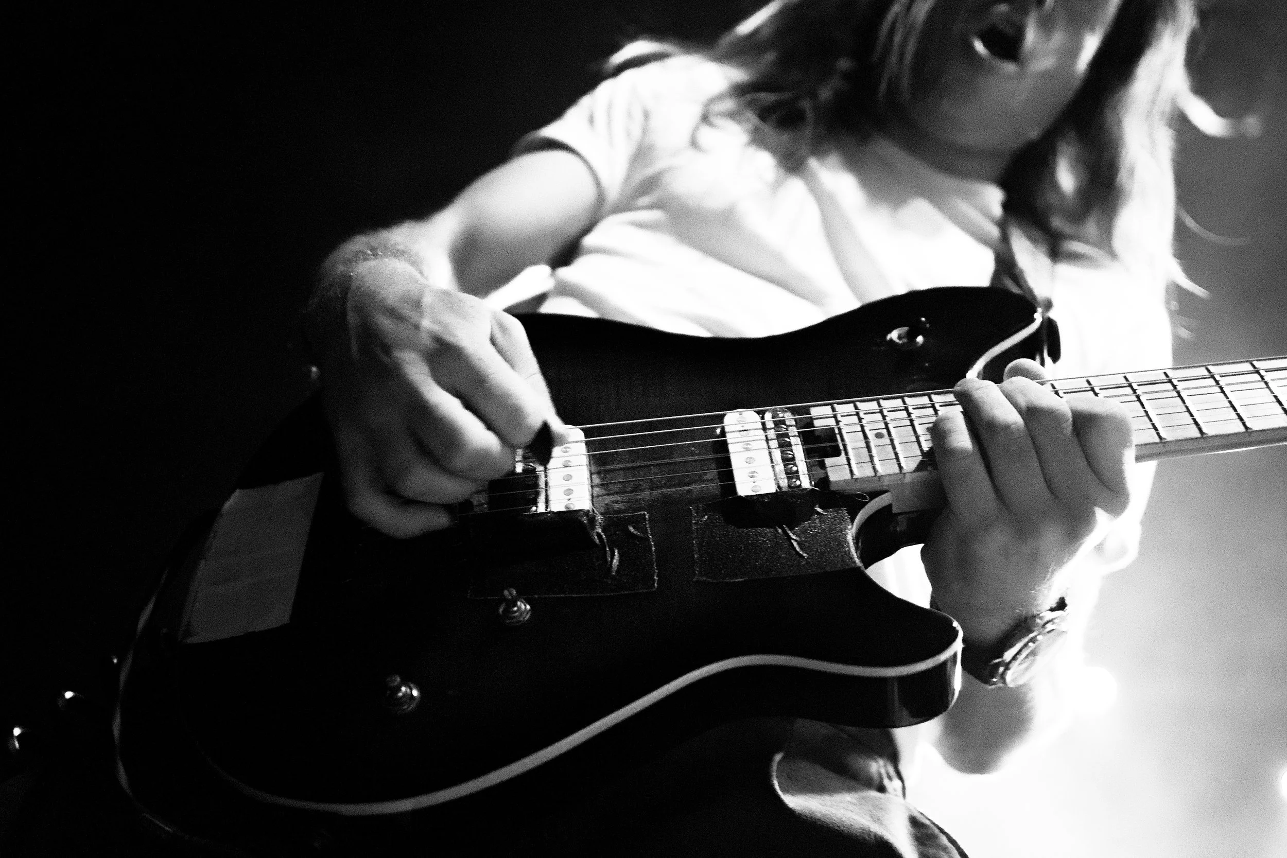 Close-up of a person playing an electric guitar, focusing on their hands and the guitar neck, in black and white.