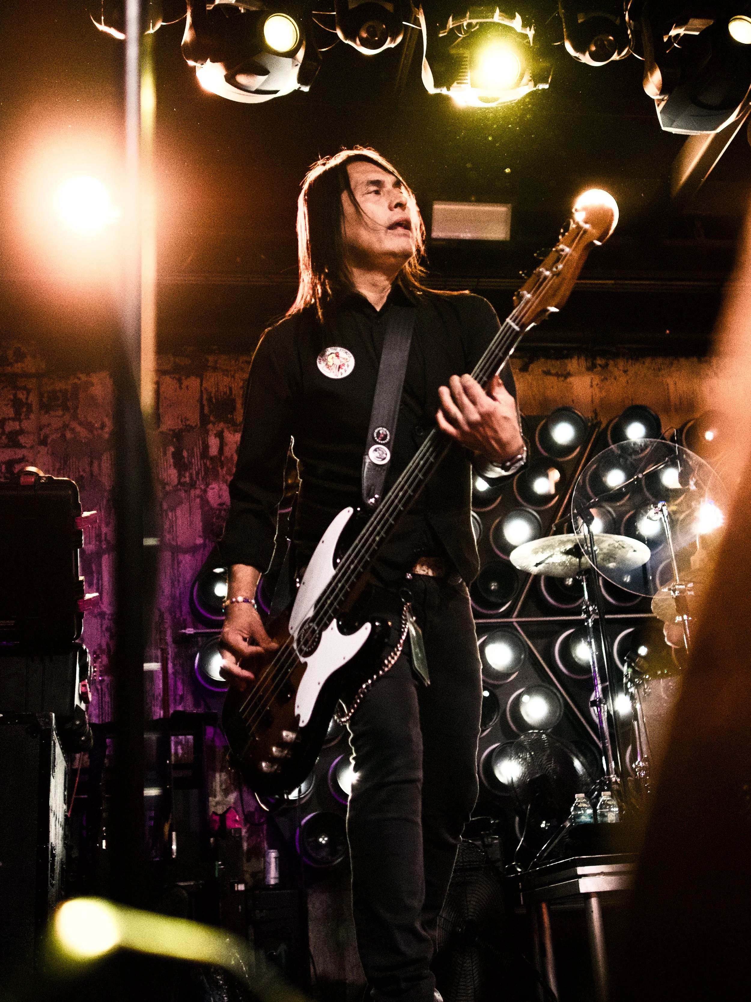 A musician playing bass guitar on stage, surrounded by stage lights and speakers.