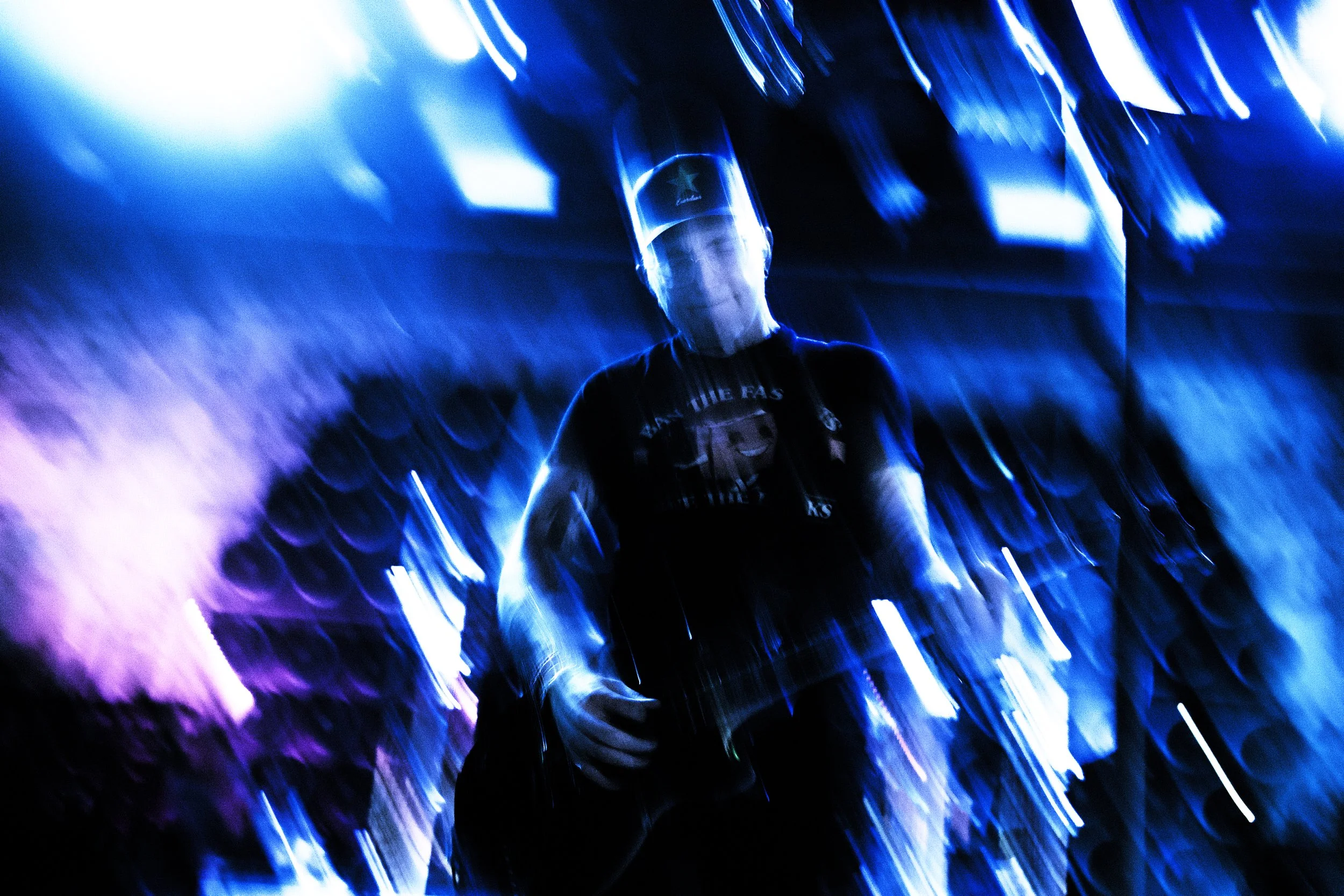 A person playing guitar in a dimly lit space surrounded by blue and purple lights, with a motion blur effect creating a dynamic, abstract appearance.