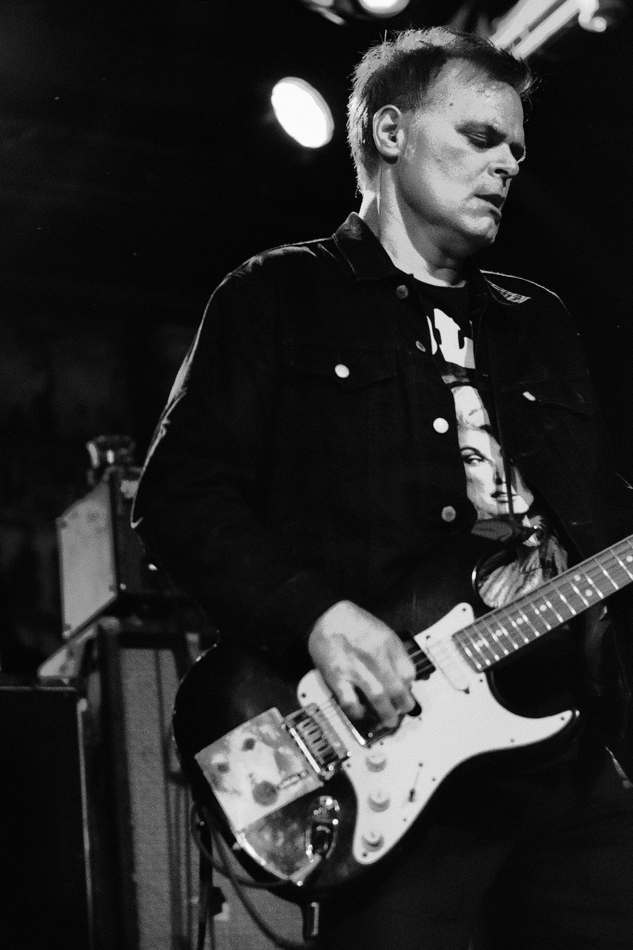 A man playing an electric guitar on stage, black and white photo.