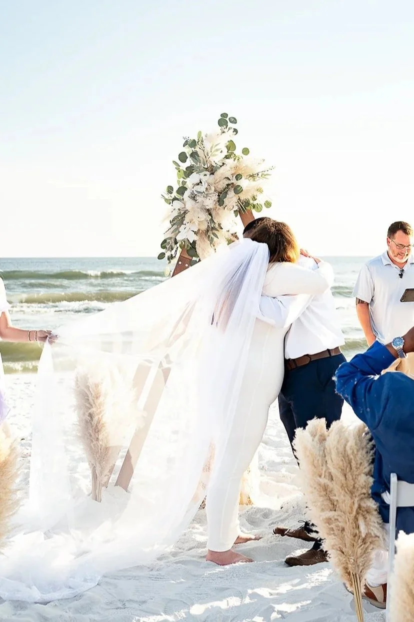 newlyweds embracing after wedding ceremony on dune allen beach with the waves crashing behind their wooden ceremony arbor