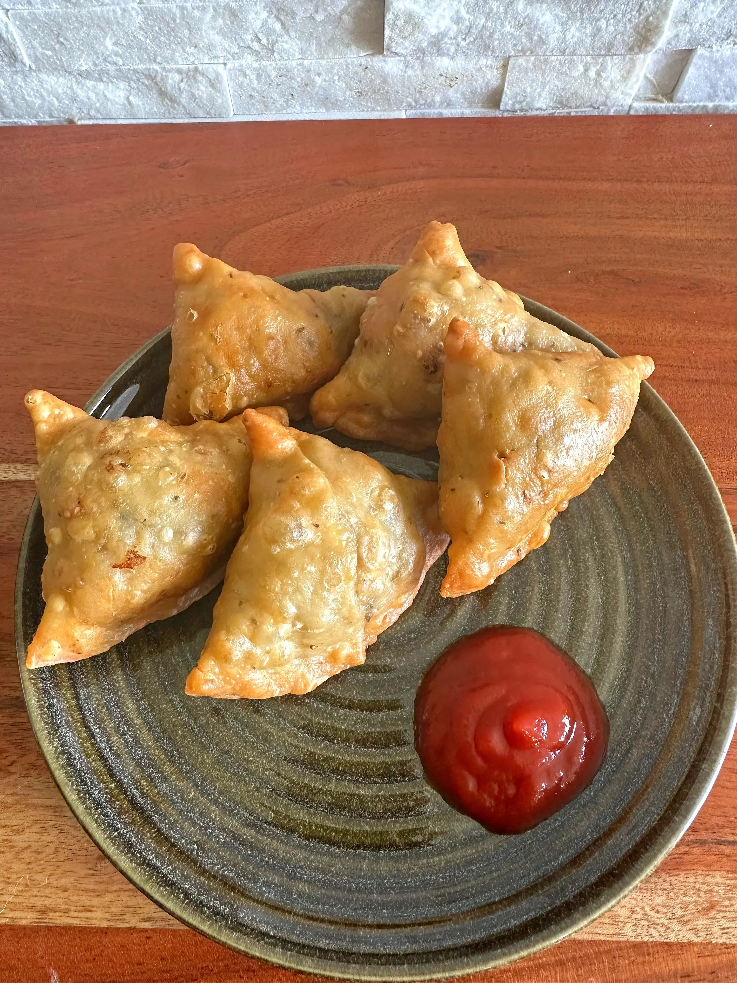 A plate with five fried samosas and a small serving of ketchup.