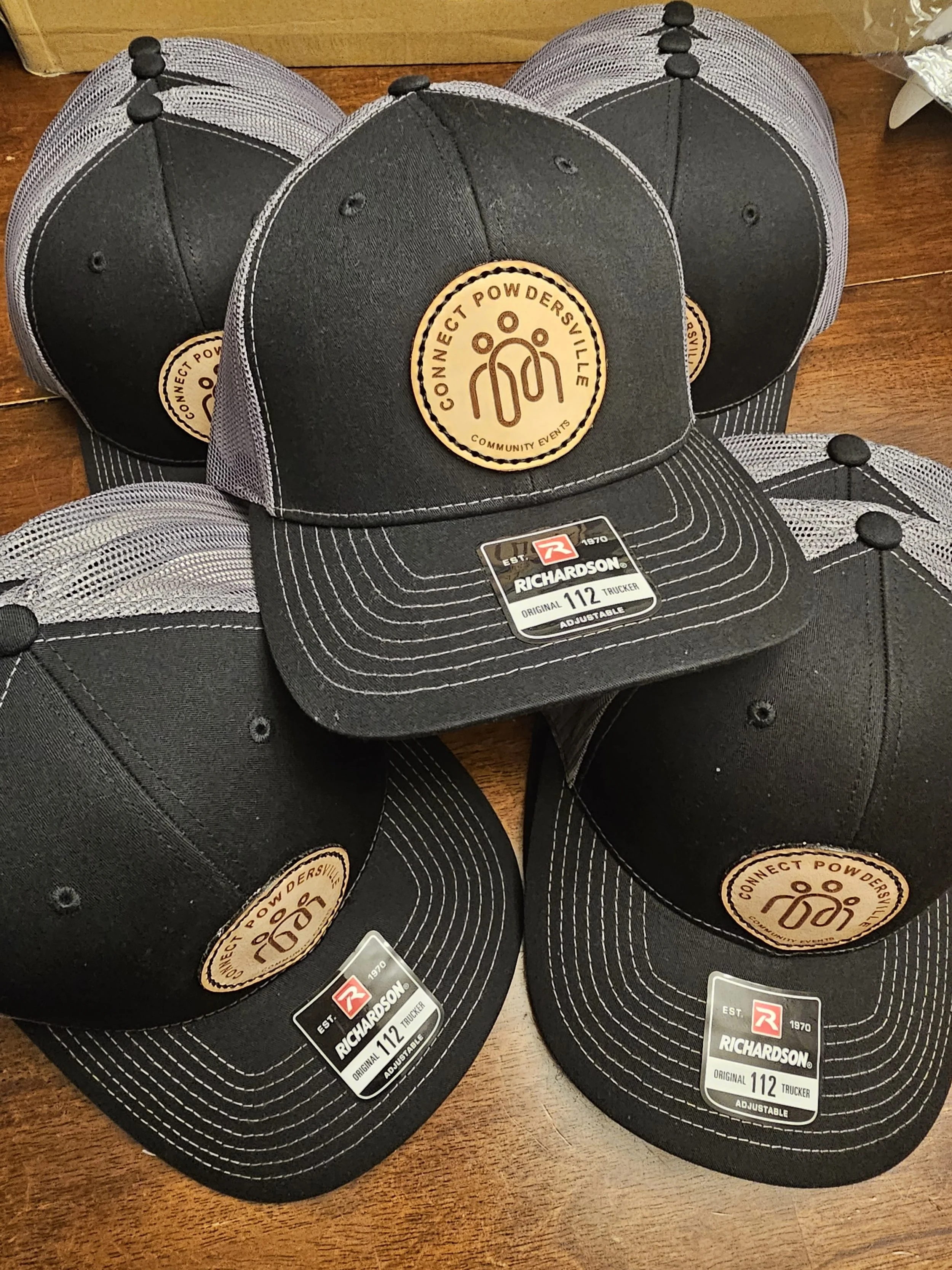 A round leather patch that is sewn on to a black/charcoal Richardson 112 hat.