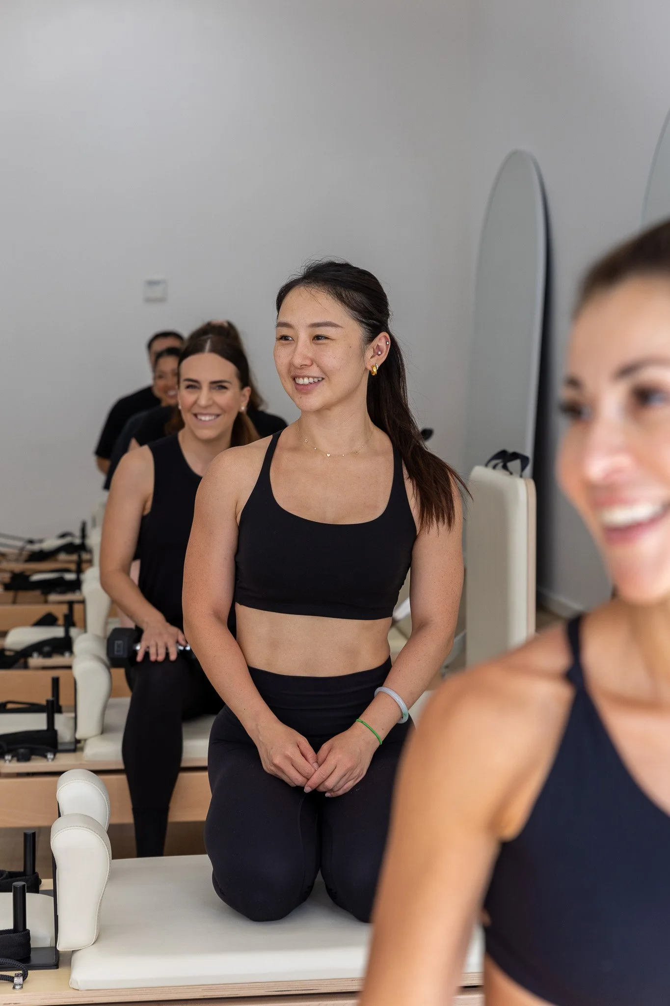 Group of women participating in a fitness or yoga class, kneeling on mats, dressed in black athletic wear, smiling and relaxed.