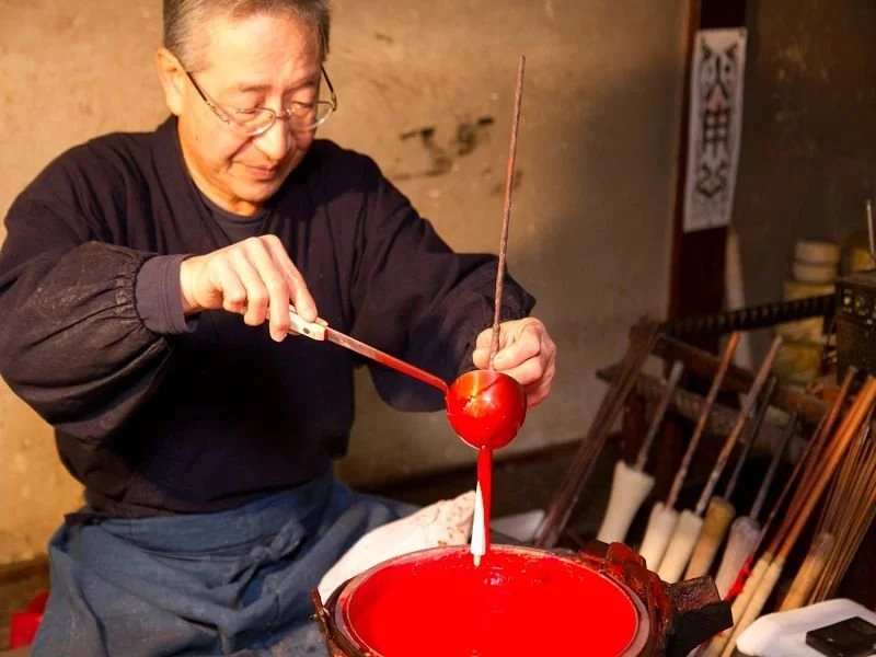 Person crafting a Japanese umbrella, applying red lacquer with a brush.