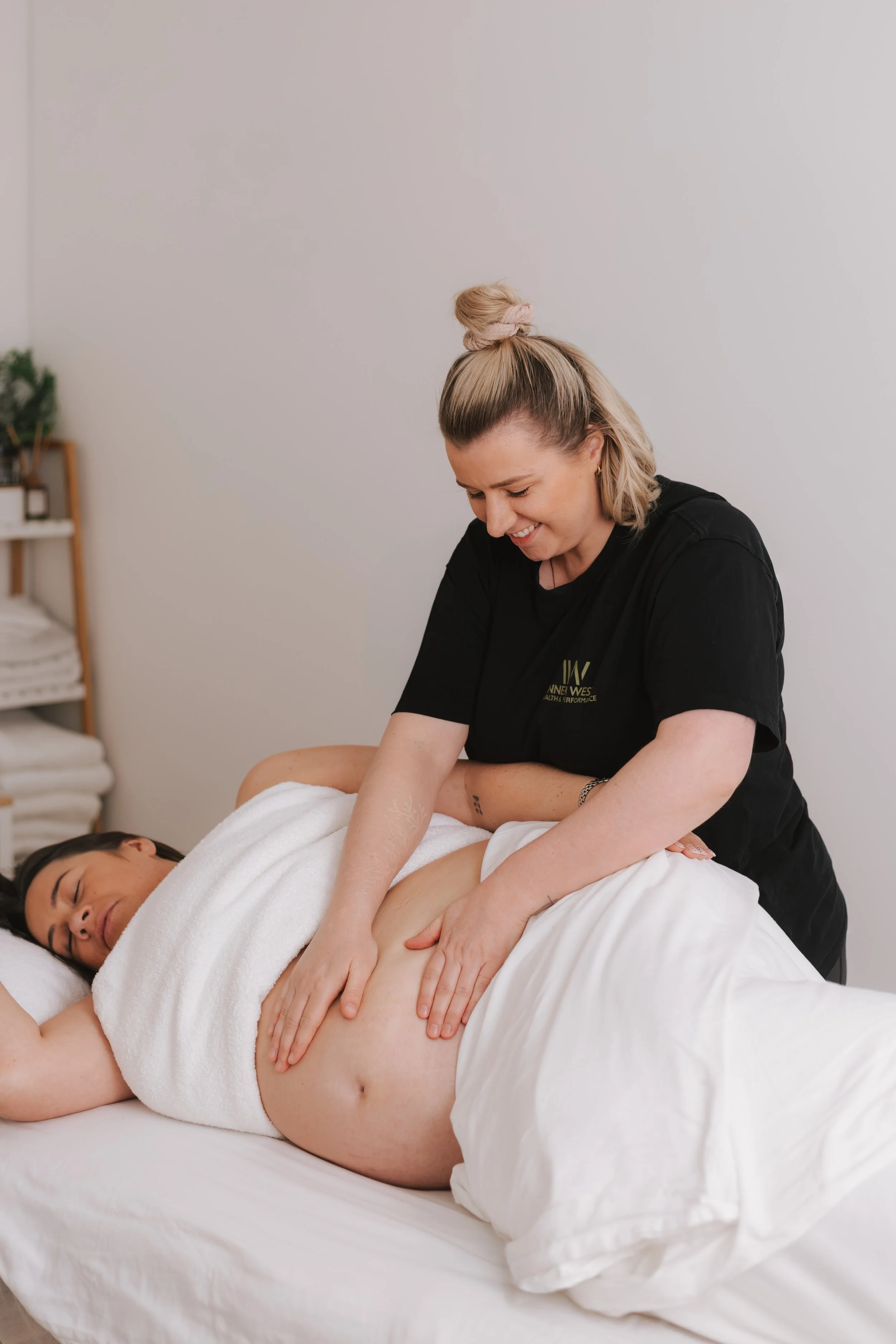 Georgie, massage therapist gently massage a pregnancy women's belly as she is in a side-lying position on a treatment table
