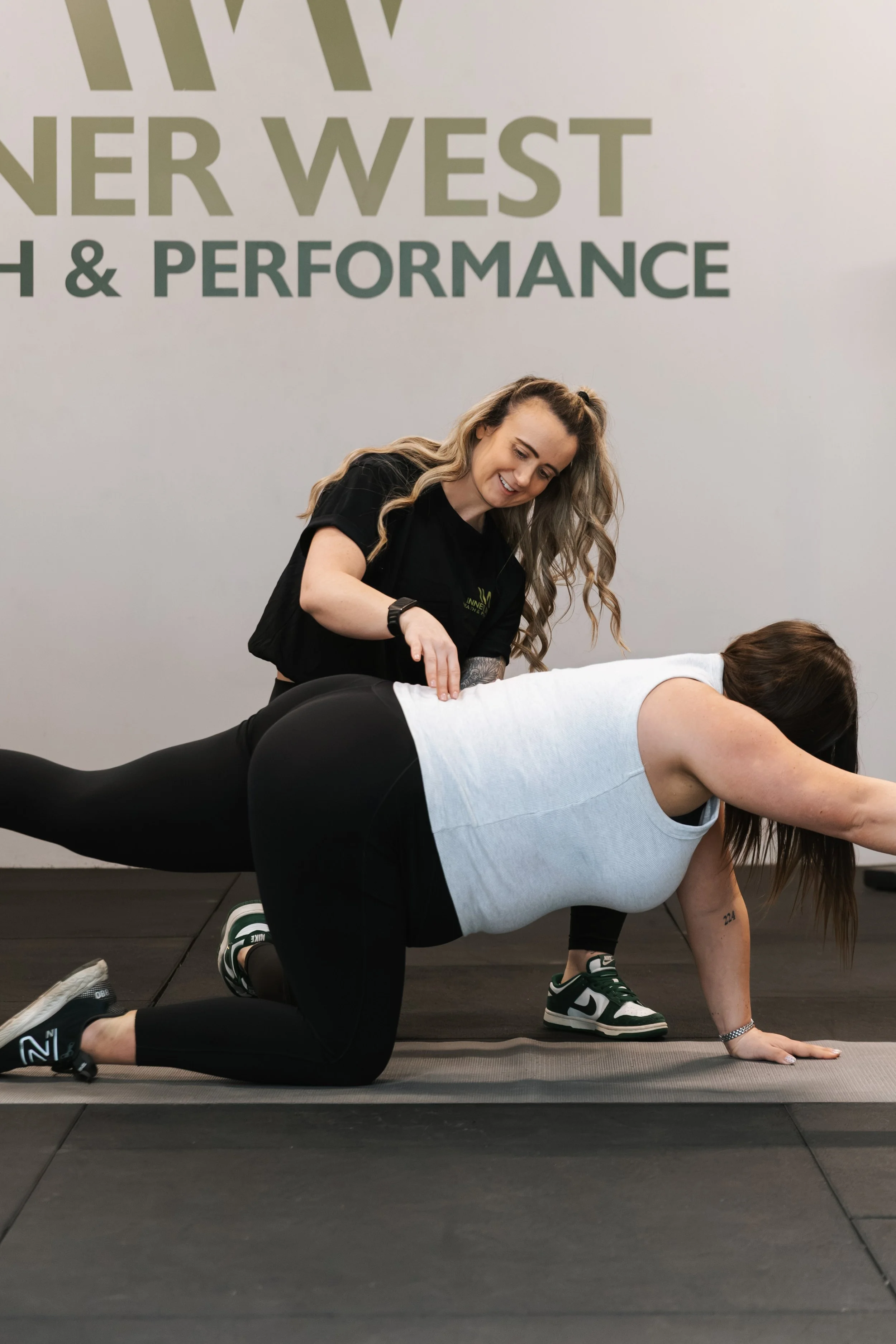Pregnant client on their hands and knees with Kirby supporting from the other side as she performs a bird dog exercise