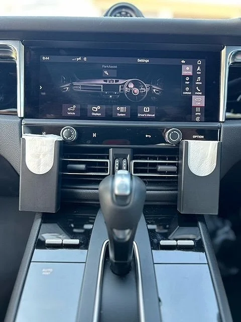 Car interior showing a touchscreen infotainment system displaying car settings, with dual cup holders and a gear shift in the foreground.
