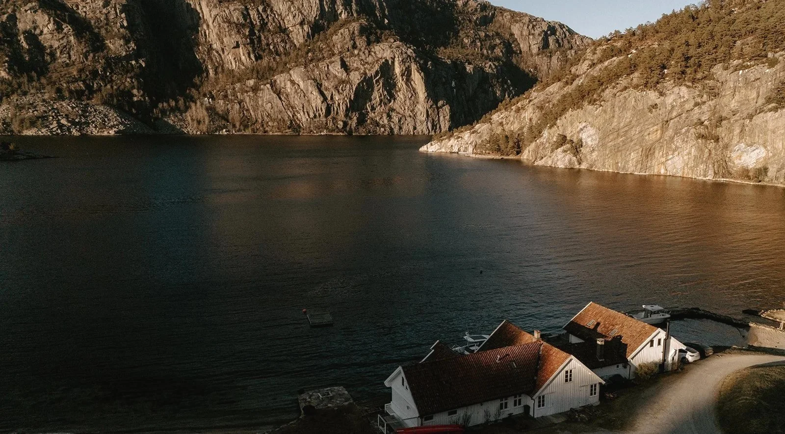 Häuser am Ufer eines Fjords mit steilen, felsigen Bergen im Hintergrund.