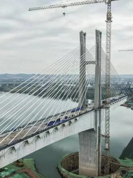 Cable-stayed bridge under construction over a river with scaffolding and cranes.