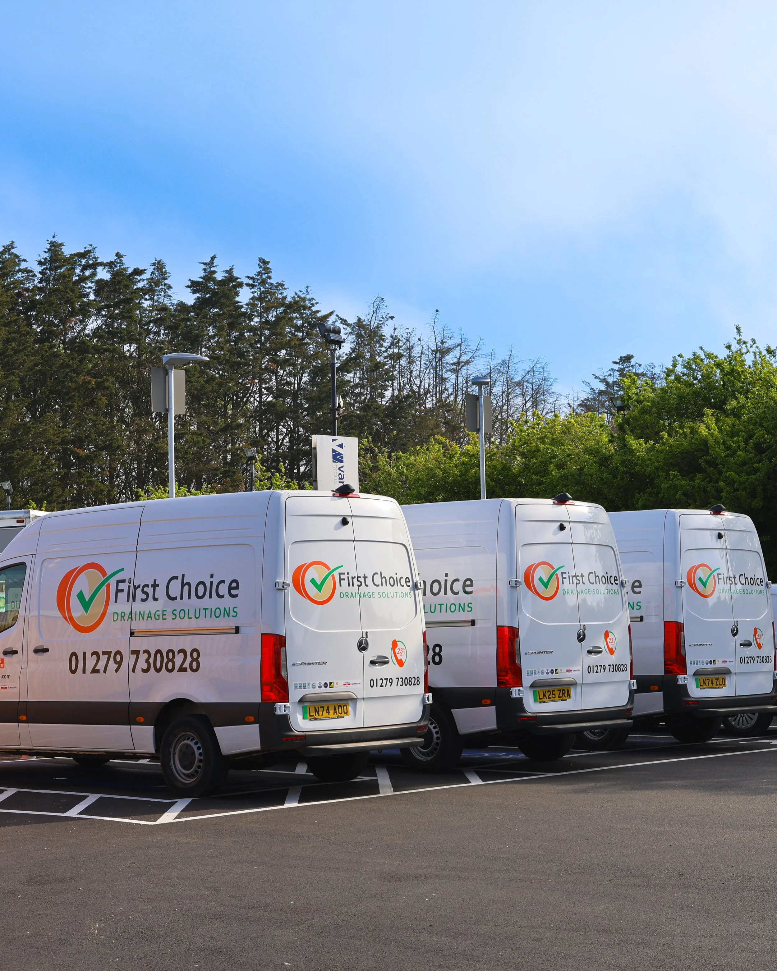 Four white vans parked in a parking lot, with