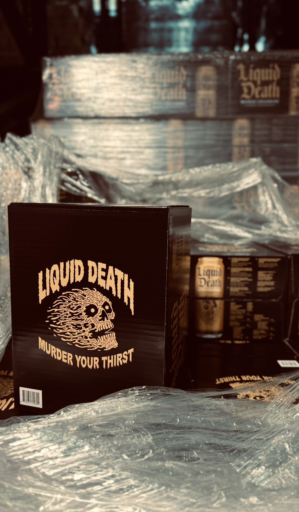 Black box labeled 'Liquid Death' with a skull design and the slogan 'Murder Your Thirst' in front of stacked boxes of the same product.