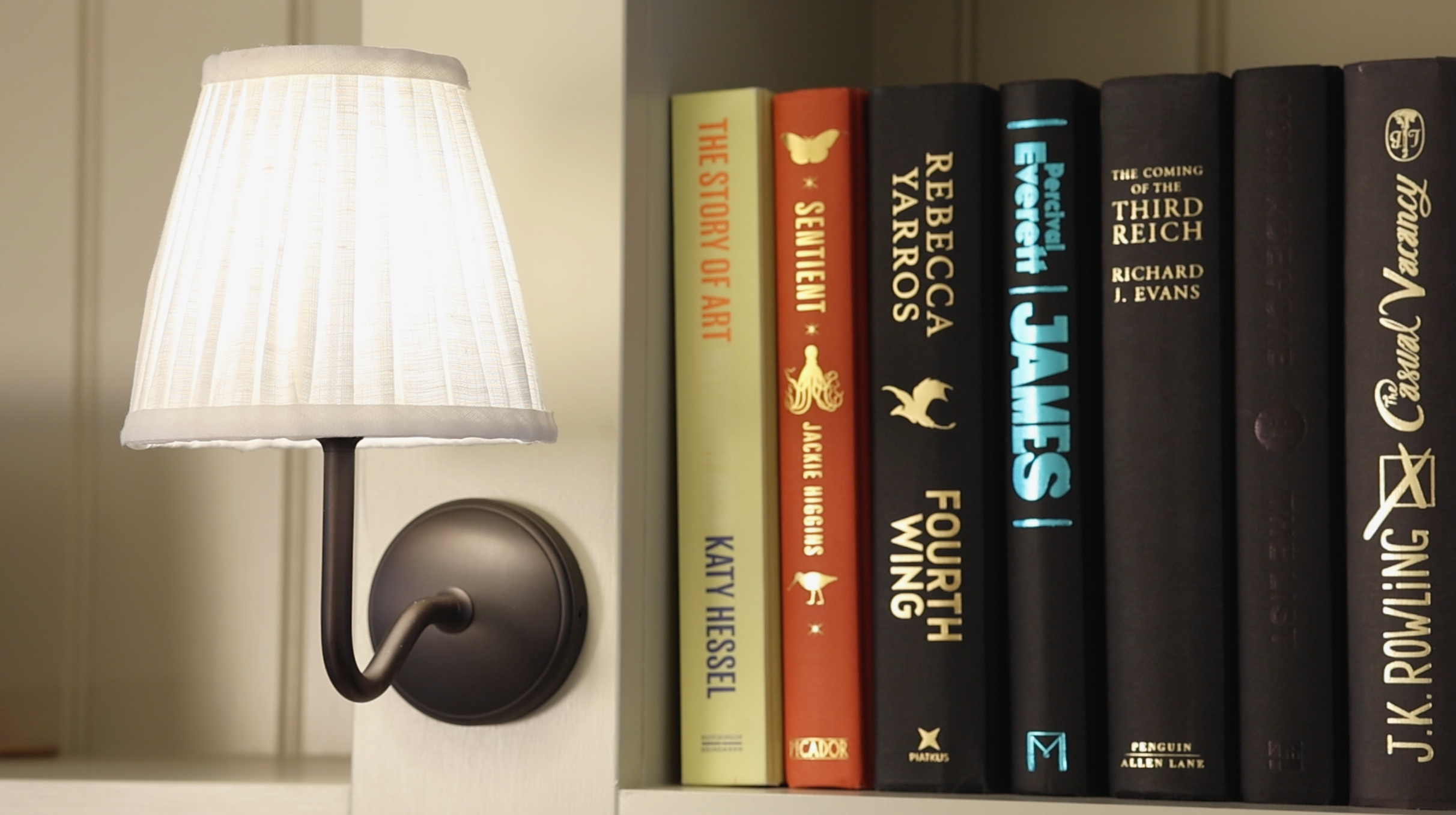 A white lampshade casting light on a bookshelf filled with books.