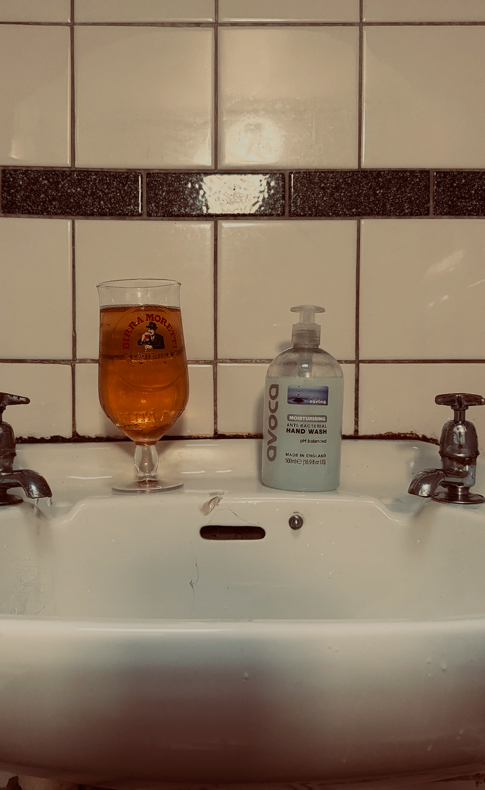 A bathroom sink with a glass of amber-colored drink and a bottle of Aveco moisturizing anti-bacterial hand wash.
