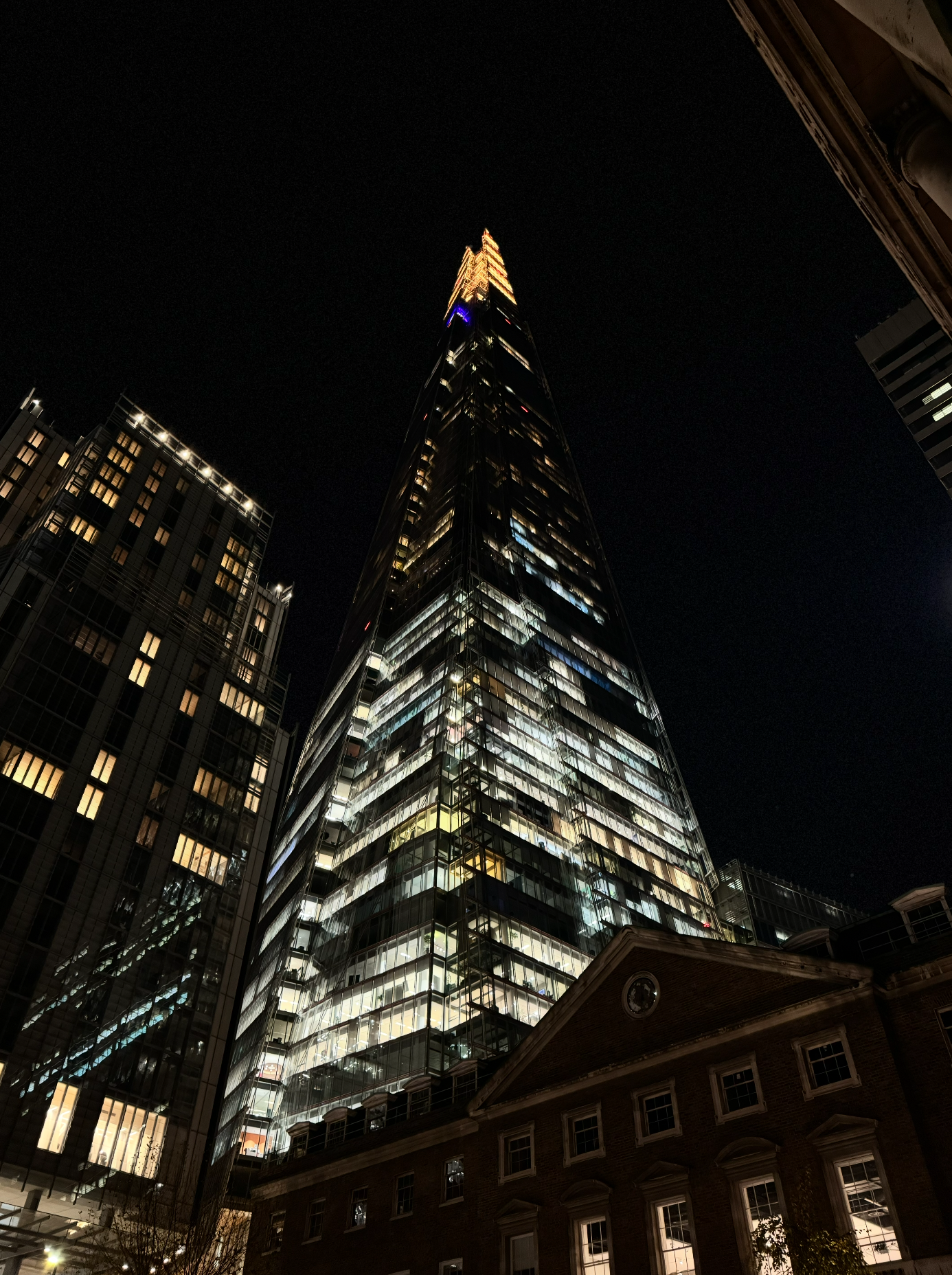 Night view of the tall, illuminated Salesforce Tower in San Francisco, California, with surrounding buildings and a dark sky above.