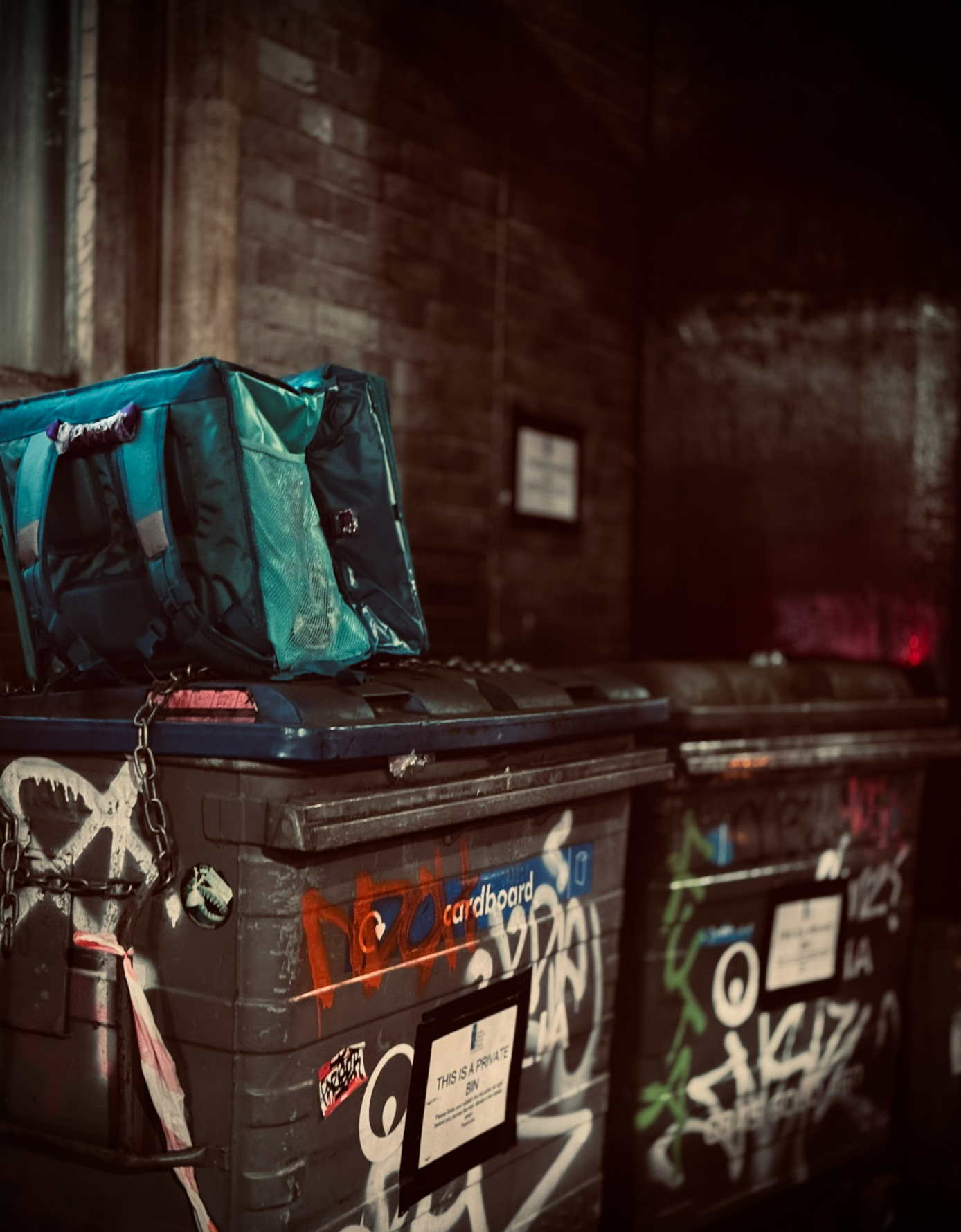 A blue backpack resting on a graffiti-covered black trash bin inside a dimly lit room with wooden walls.