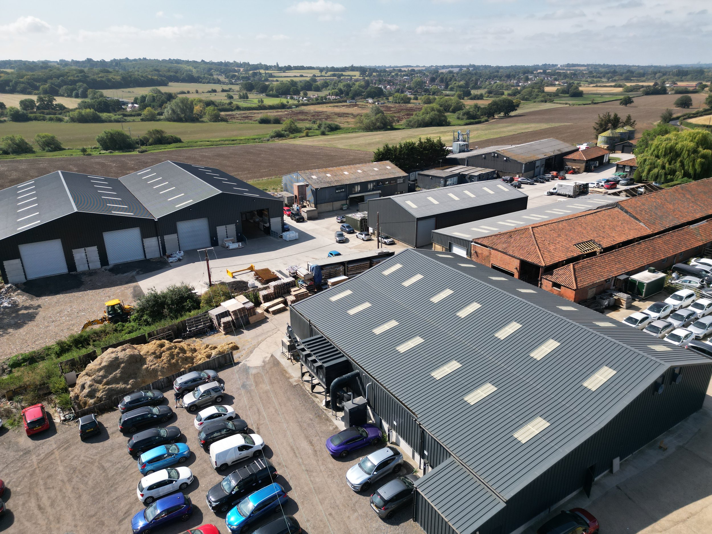 An aerial view of an industrial area with multiple warehouses and buildings, surrounded by green fields and open landscape.