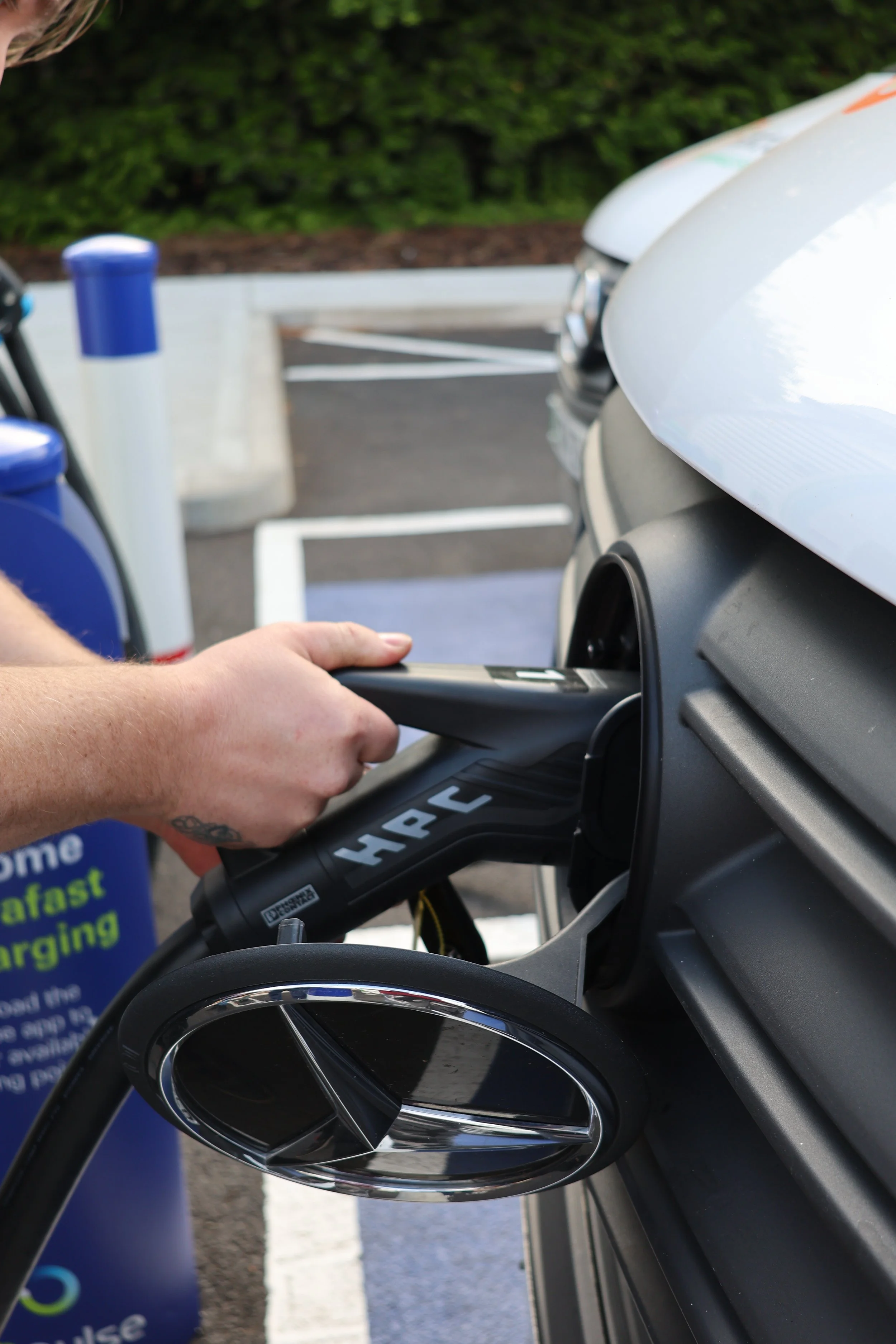 Person charging an electric car using a handheld charger at a parking lot.