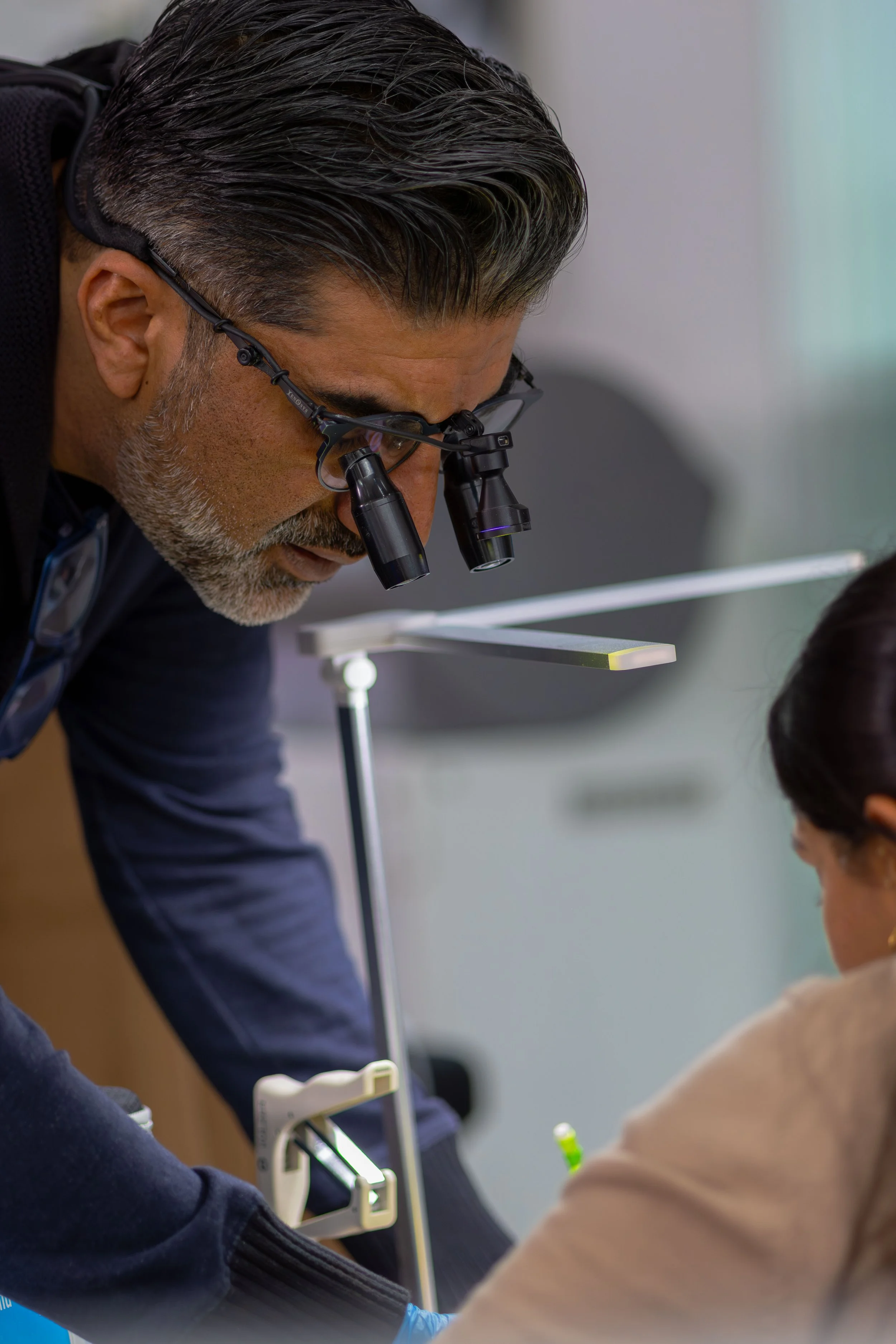 A male doctor with gray hair and glasses examining a young child's ear with specialized medical equipment in a clinic.