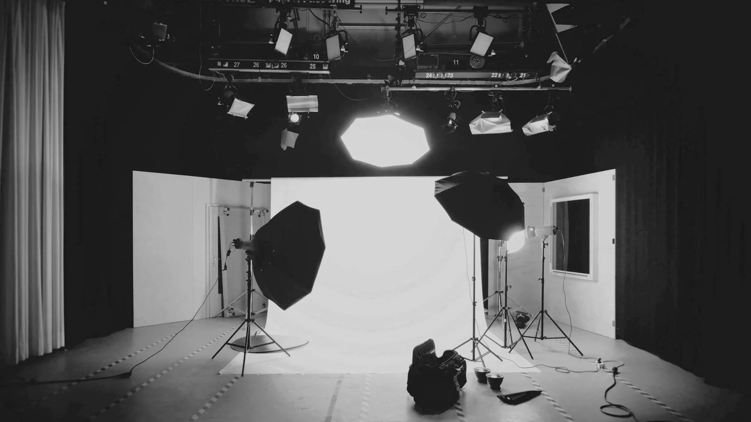 Photogram of a professional photography studio with lighting equipment, a white backdrop, and a camera bag on the floor.