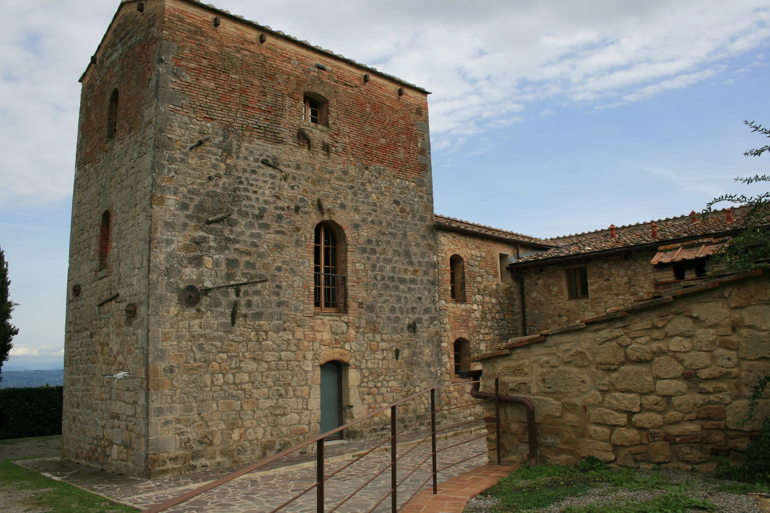 A stone and brick medieval tower with narrow windows, part of a historic building against a partly cloudy sky.