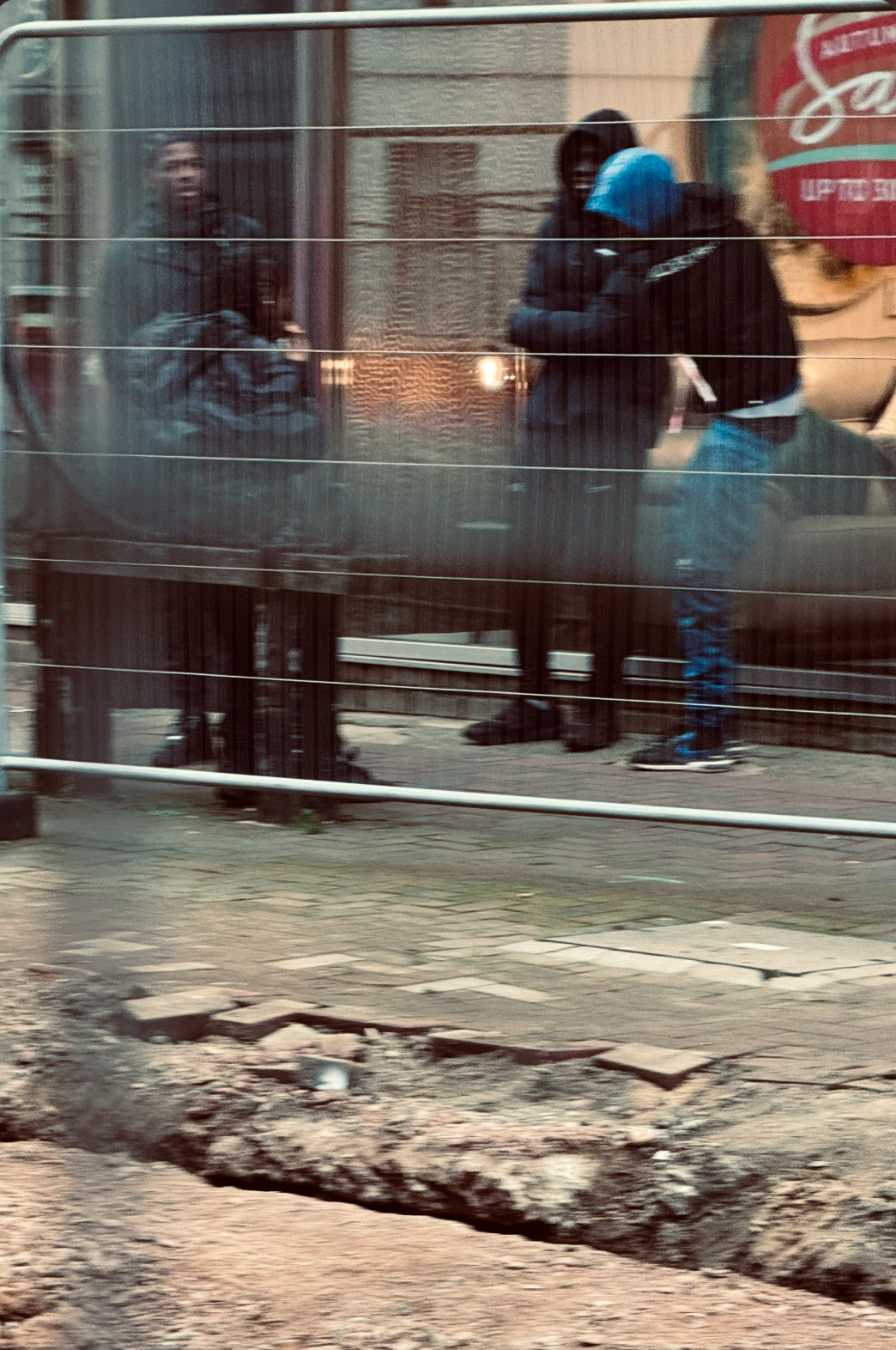 Reflected image of three people standing outside a building through a window with horizontal blinds, with a sidewalk and damaged curb in the foreground.