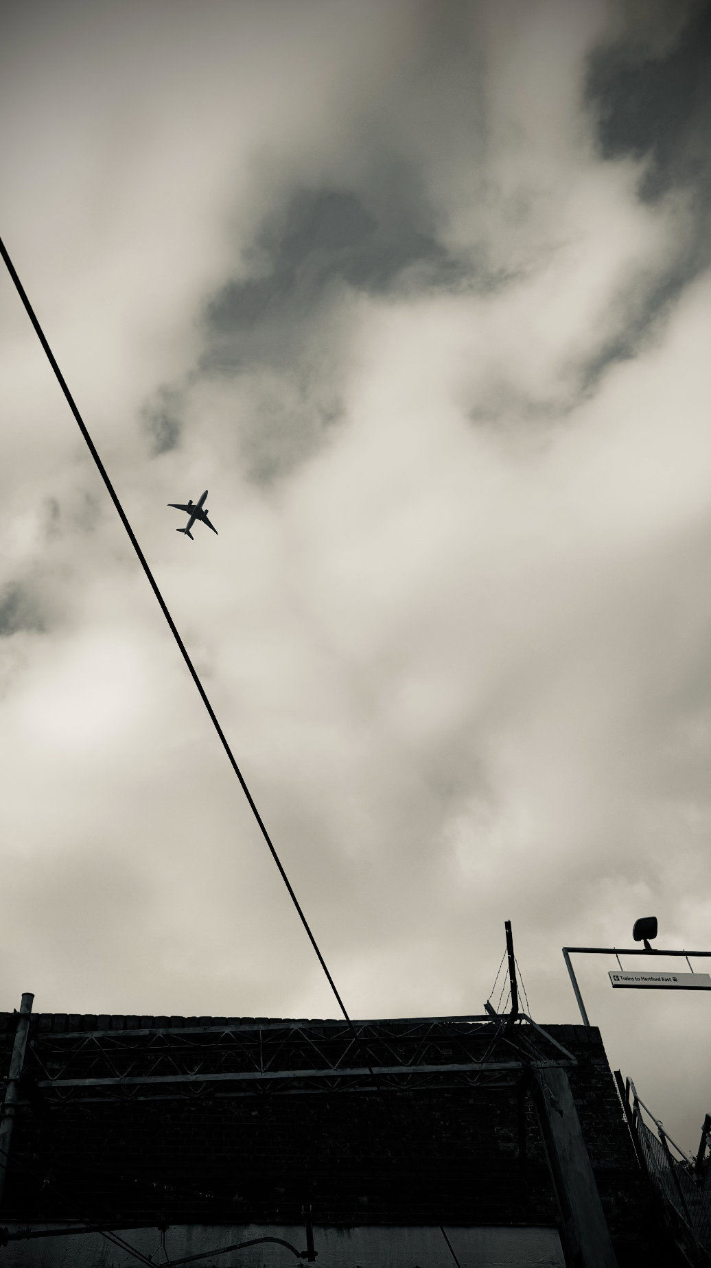 An airplane flying in cloudy, overcast sky above a building with electrical wires.
