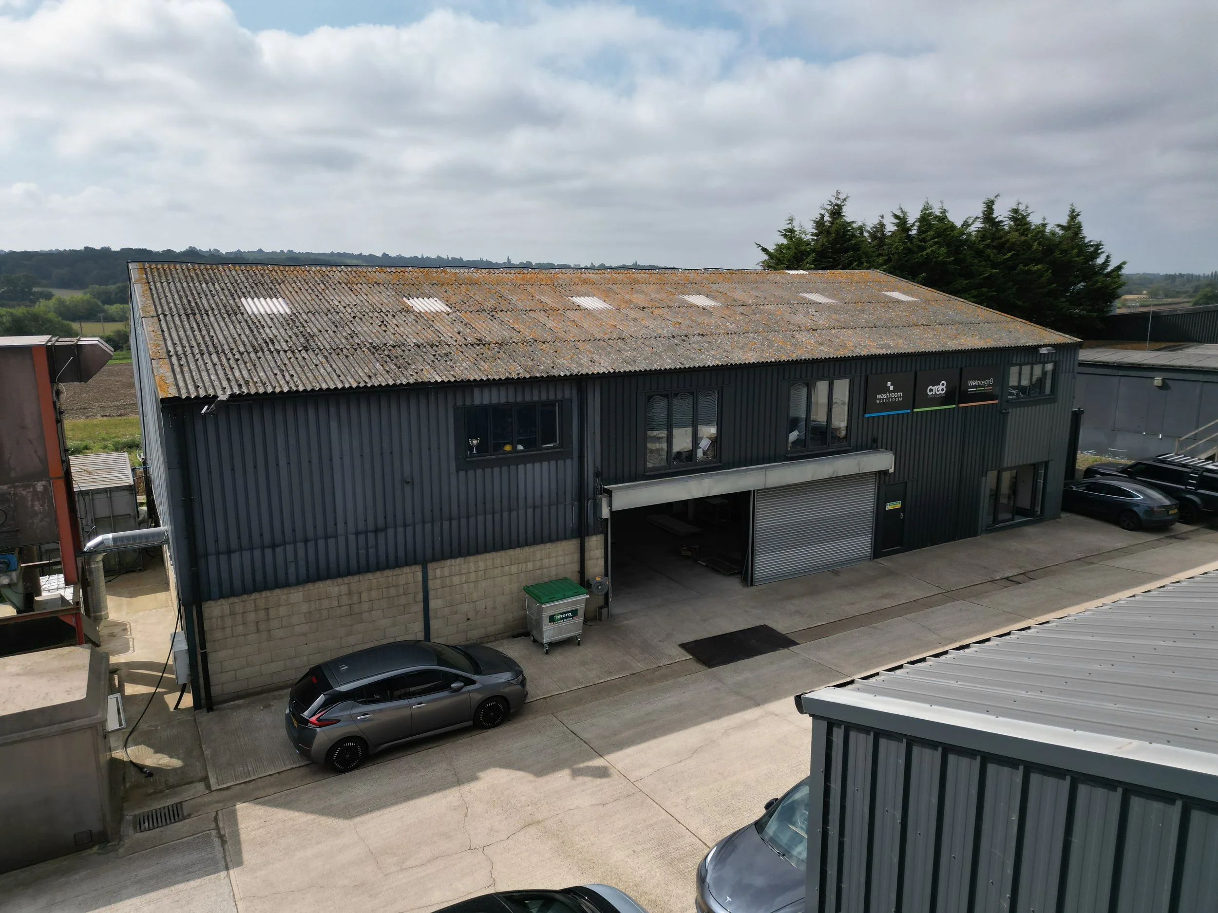 Industrial building with a rusty roof, dark exterior walls, and several parked cars outside.
