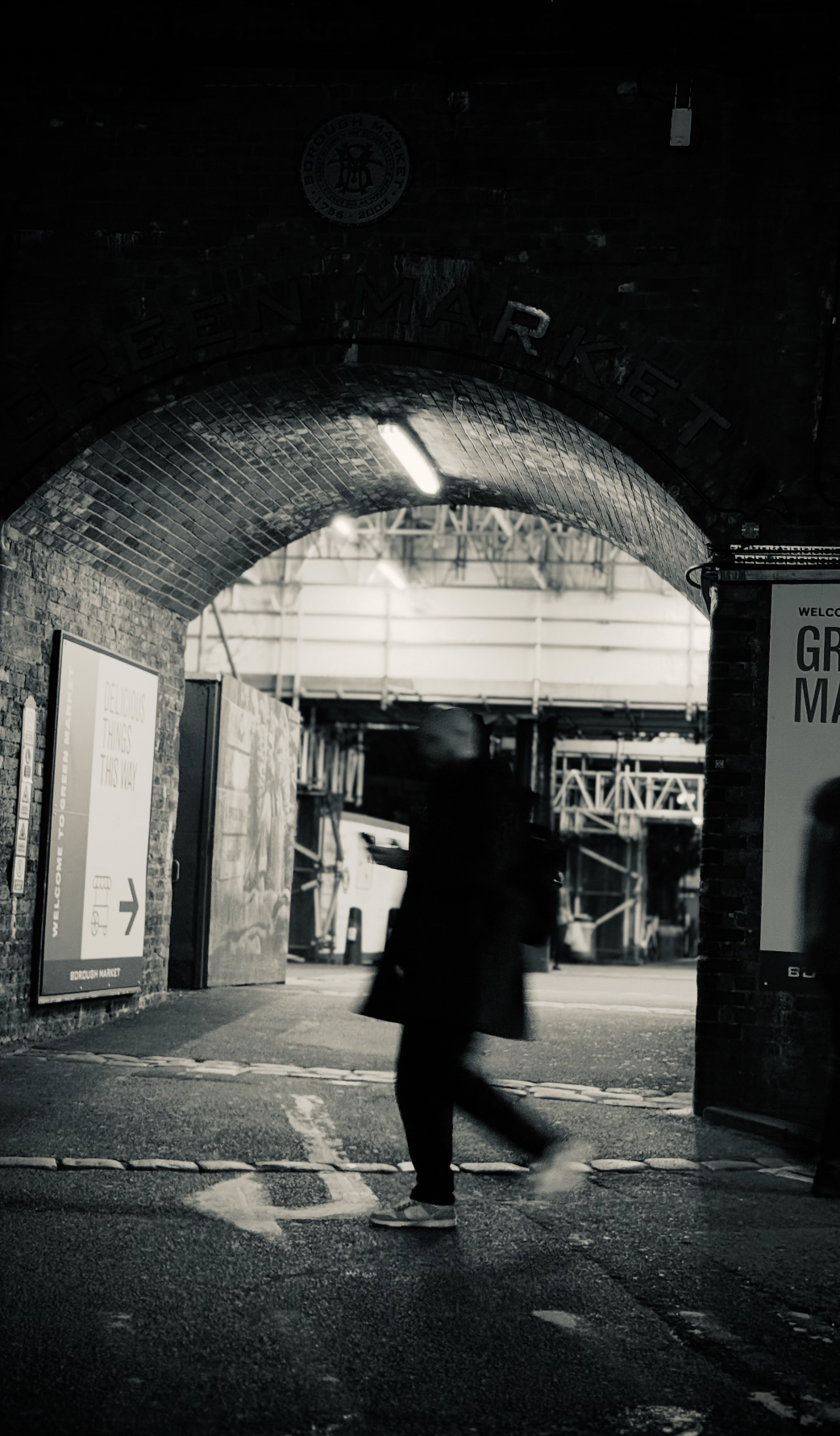 A person walking through an underpass at Borough Market, with signs and construction in the background, in black and white.