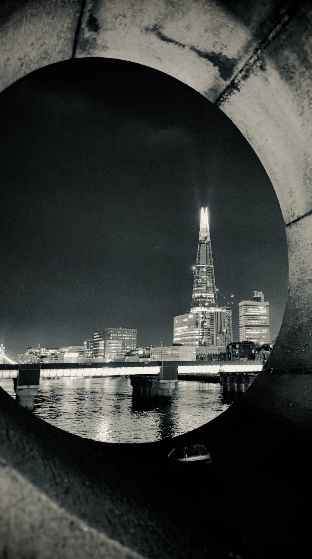 Night view of the London skyline, featuring The Shard, seen through a circular opening in a stone structure.