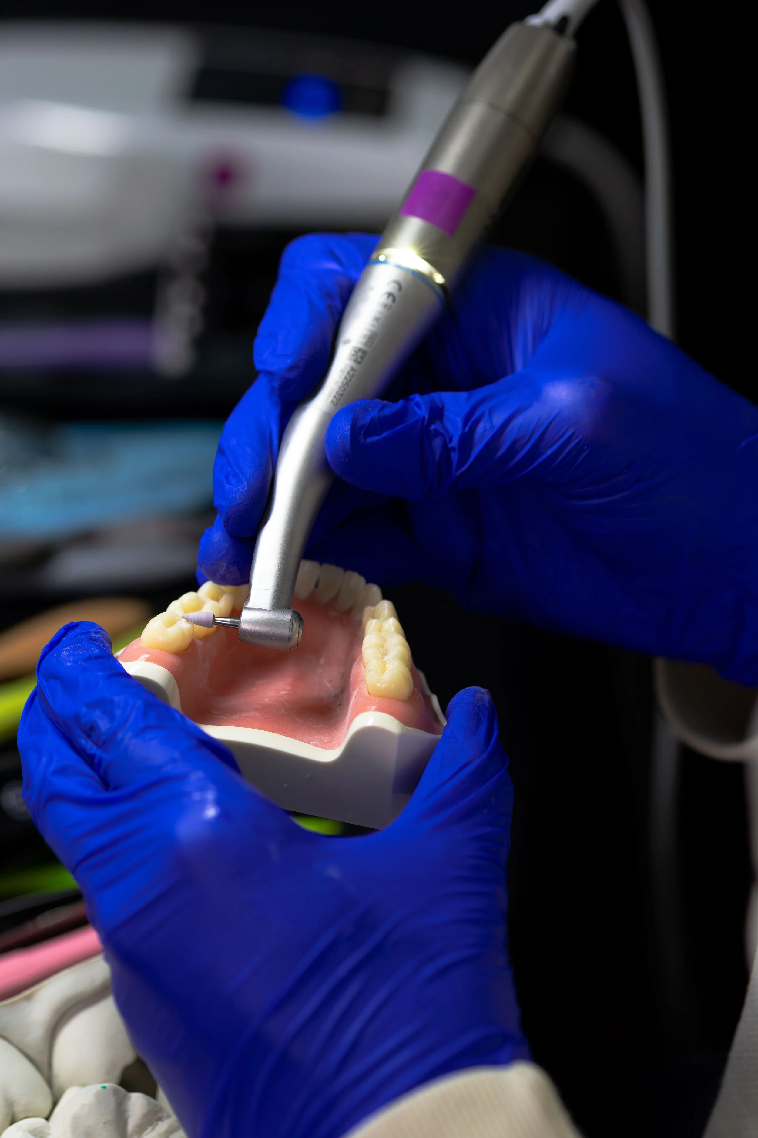 A person wearing blue gloves working with a dental model and a dental handpiece for dental procedures.
