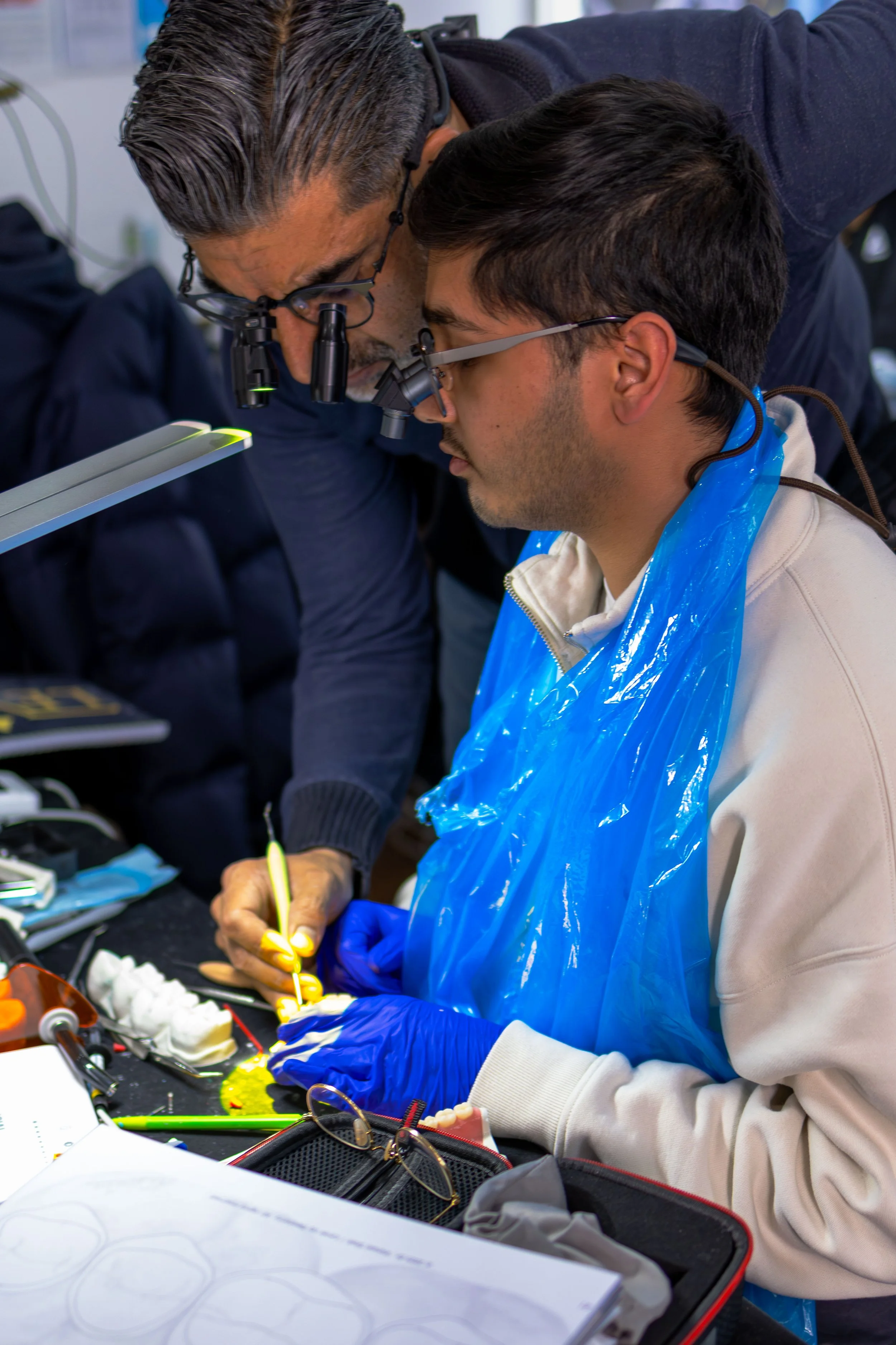 Two scientists or engineers in a laboratory examining a small object with magnifying glasses and tools, wearing gloves and protective gear.