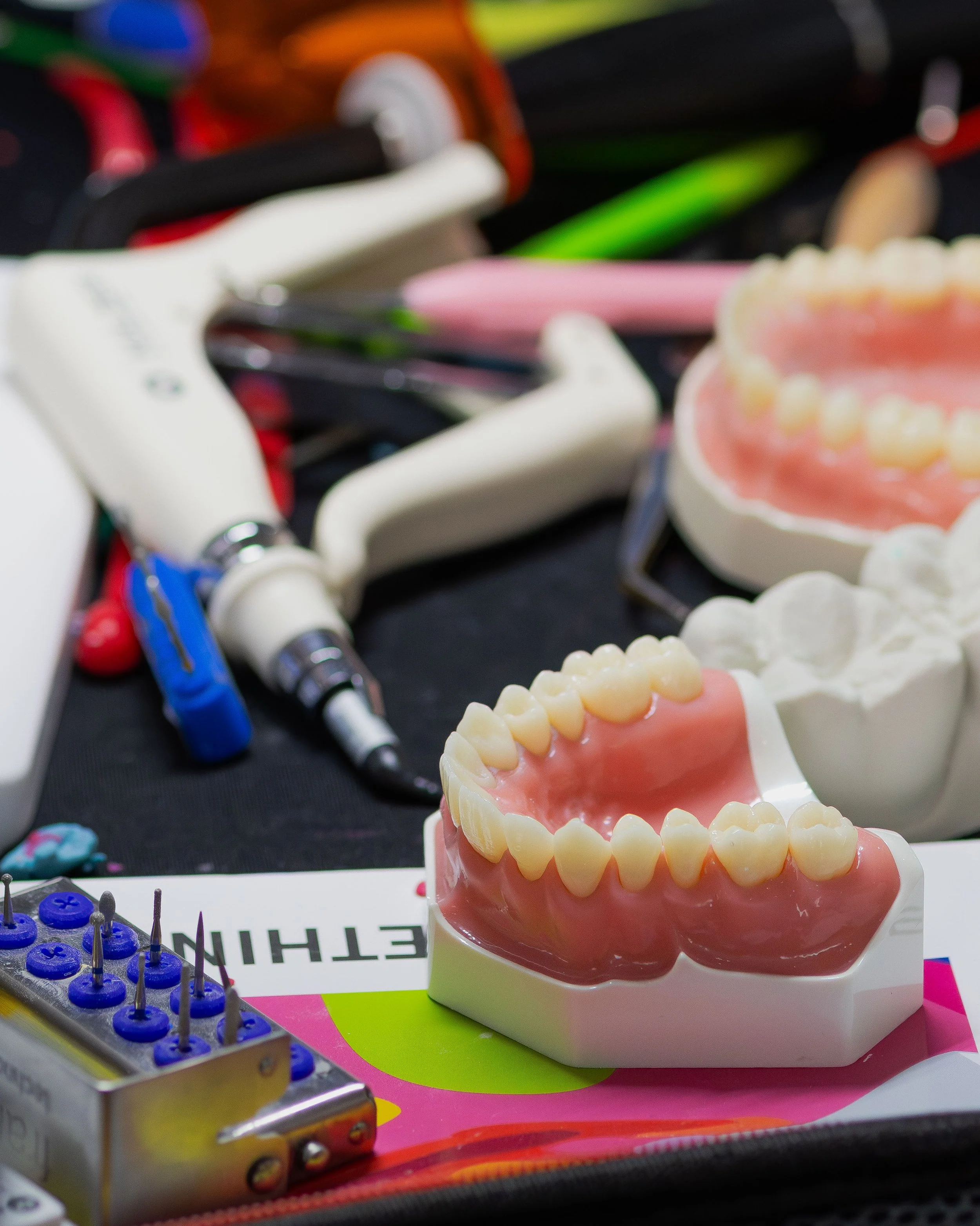 Close-up of dental model with artificial teeth, dental tools, and a dental drill in the background.