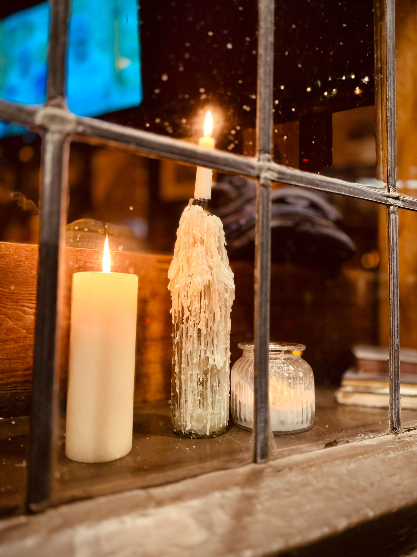 Candles and candles jars on a windowsill behind metal bars with a colorful stained glass window in the background.