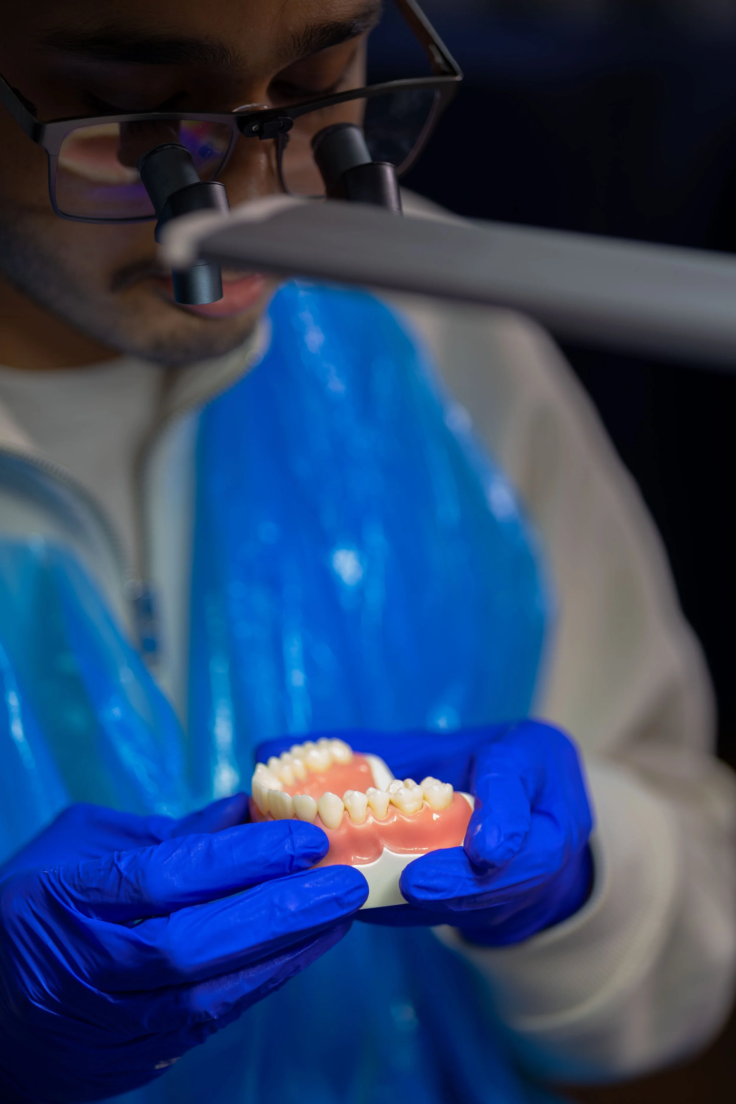 A person wearing glasses and blue gloves is examining or demonstrating dental prosthetics or dentures.